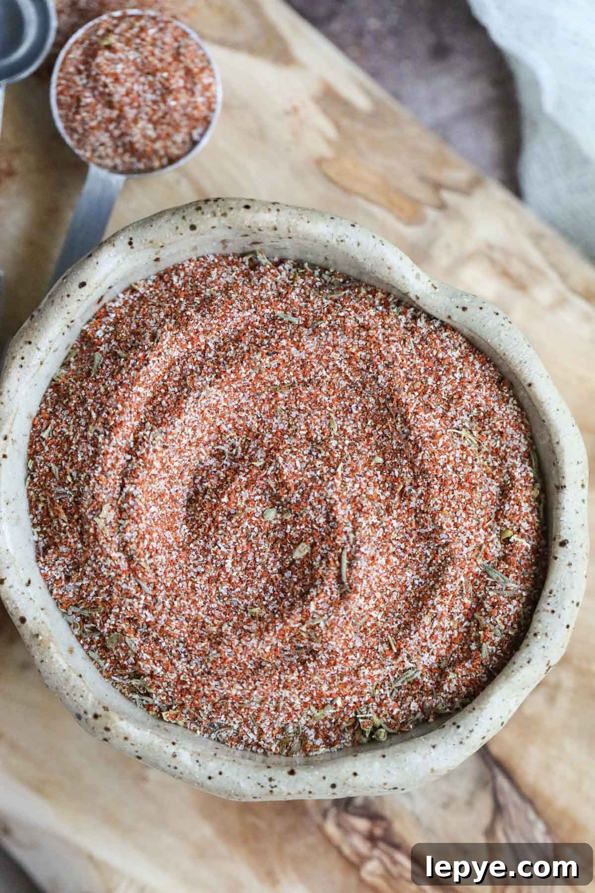 cajun seasoning in a brown bowl on a wooden cutting board.