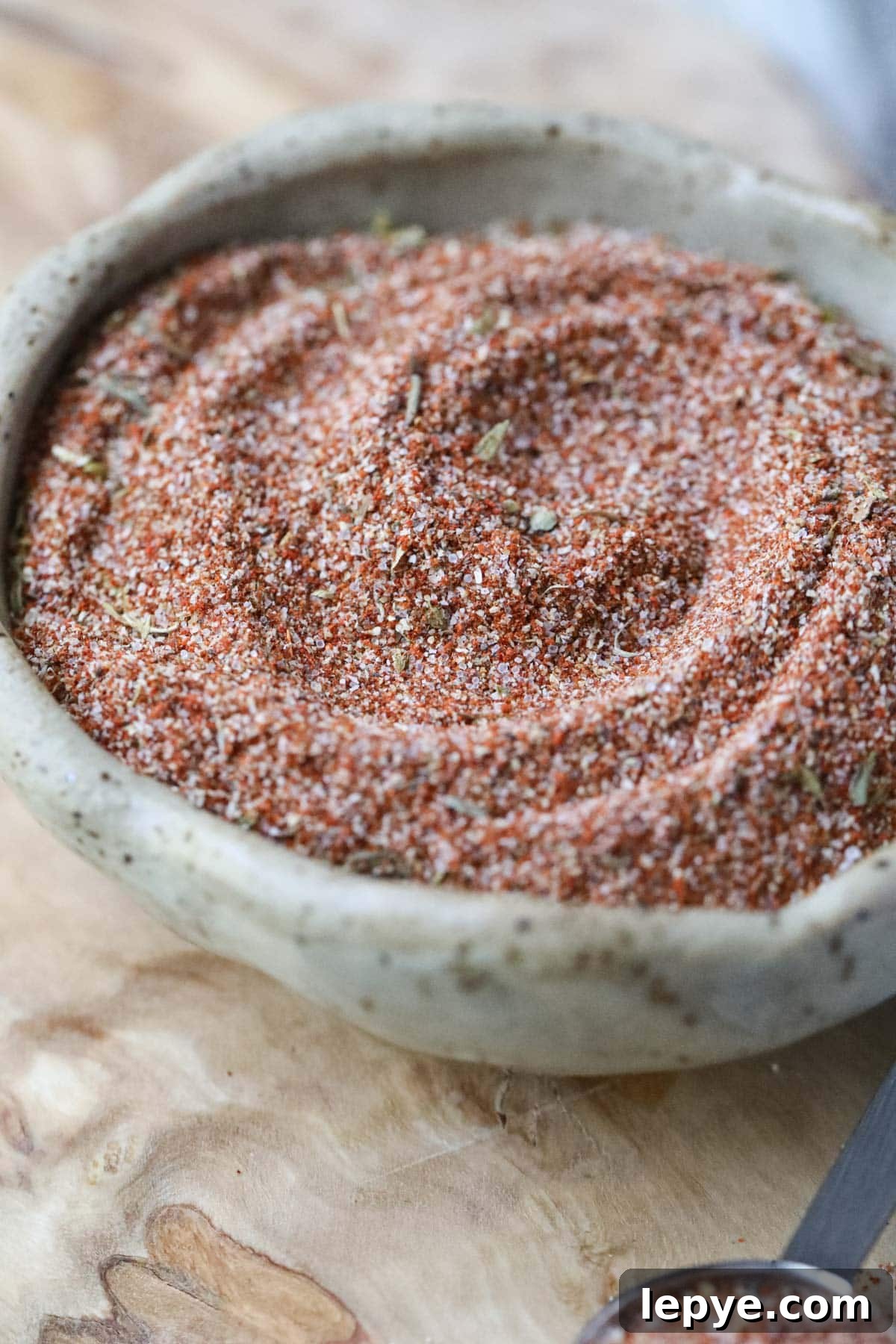 cajun seasoning in a brown bowl on a wooden cutting board.