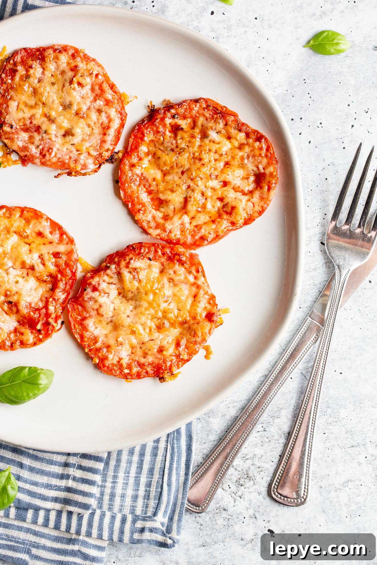 Crispy Parmesan Air Fryer Tomatoes Recipe 2 Roasted tomatoes with parmesan cheese on a white plate.