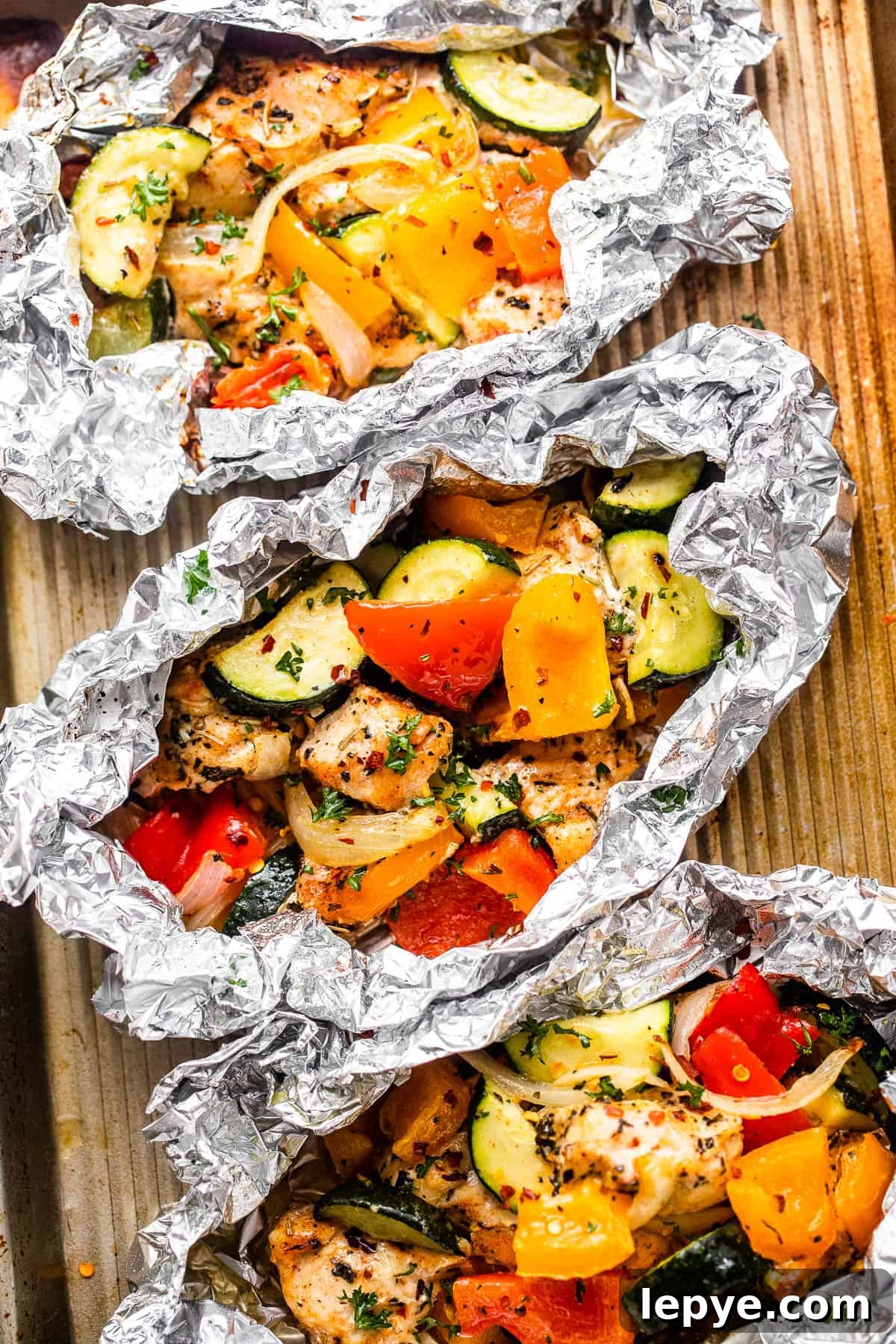 Chicken and Vegetables in Foil Packets combine juicy chicken and crisp veggies, all cooked together in foils for a convenient family meal. overhead shot of diced chicken, sliced zucchini, and sliced peppers all layered in an aluminum foil packets.