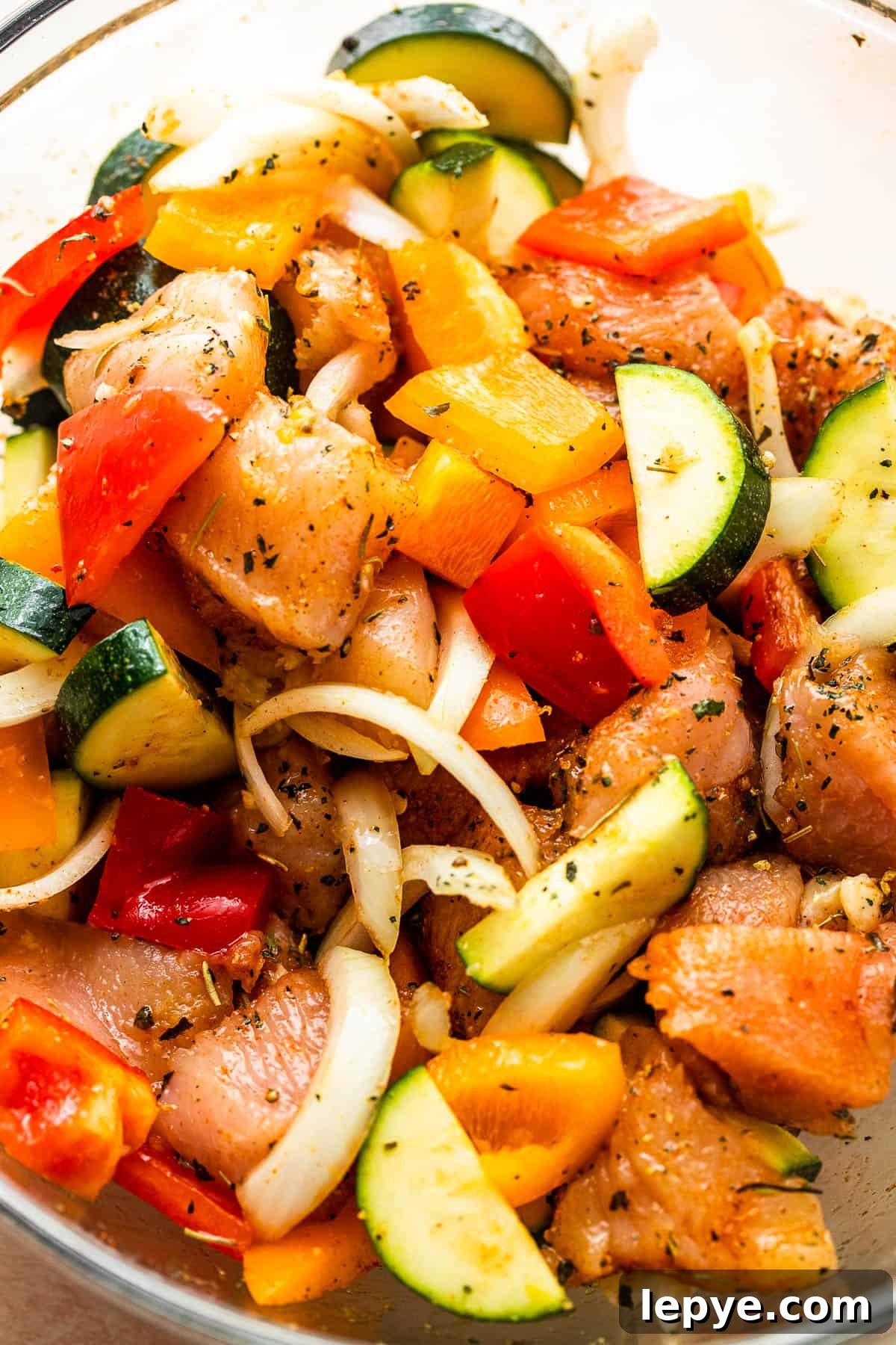 Chicken and Vegetables in Foil Packets combine juicy chicken and crisp veggies, all cooked together in foils for a convenient family meal. chicken pieces, sliced zucchini, peppers, and onions in a glass mixing bowl.