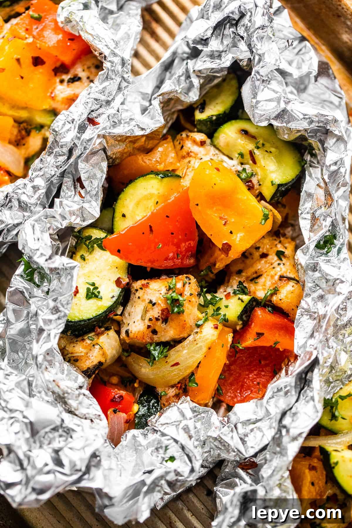 Chicken and Vegetables in Foil Packets combine juicy chicken and crisp veggies, all cooked together in foils for a convenient family meal. overhead shot of diced chicken, sliced zucchini, and sliced peppers all layered in an aluminum foil packet.