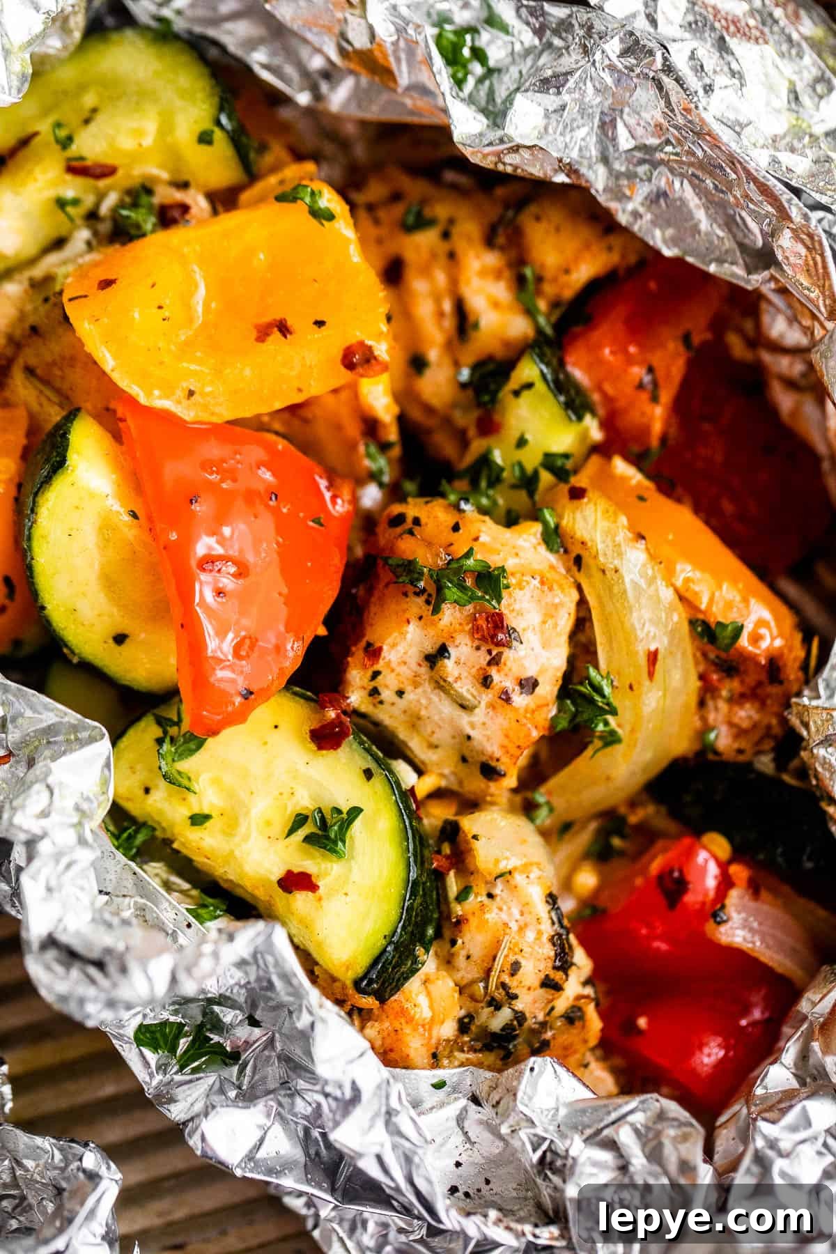 Chicken and Vegetables in Foil Packets combine juicy chicken and crisp veggies, all cooked together in foils for a convenient family meal. up close shot of diced chicken, sliced zucchini, and sliced peppers all layered in an aluminum foil packet.