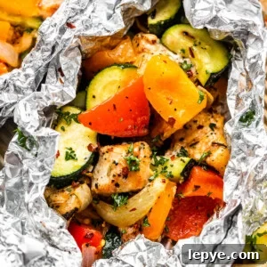 Foil-Packet Chicken with Roasted Vegetables for Quick Dinners 2 overhead shot of diced chicken, sliced zucchini, and sliced peppers all layered in an aluminum foil packet.