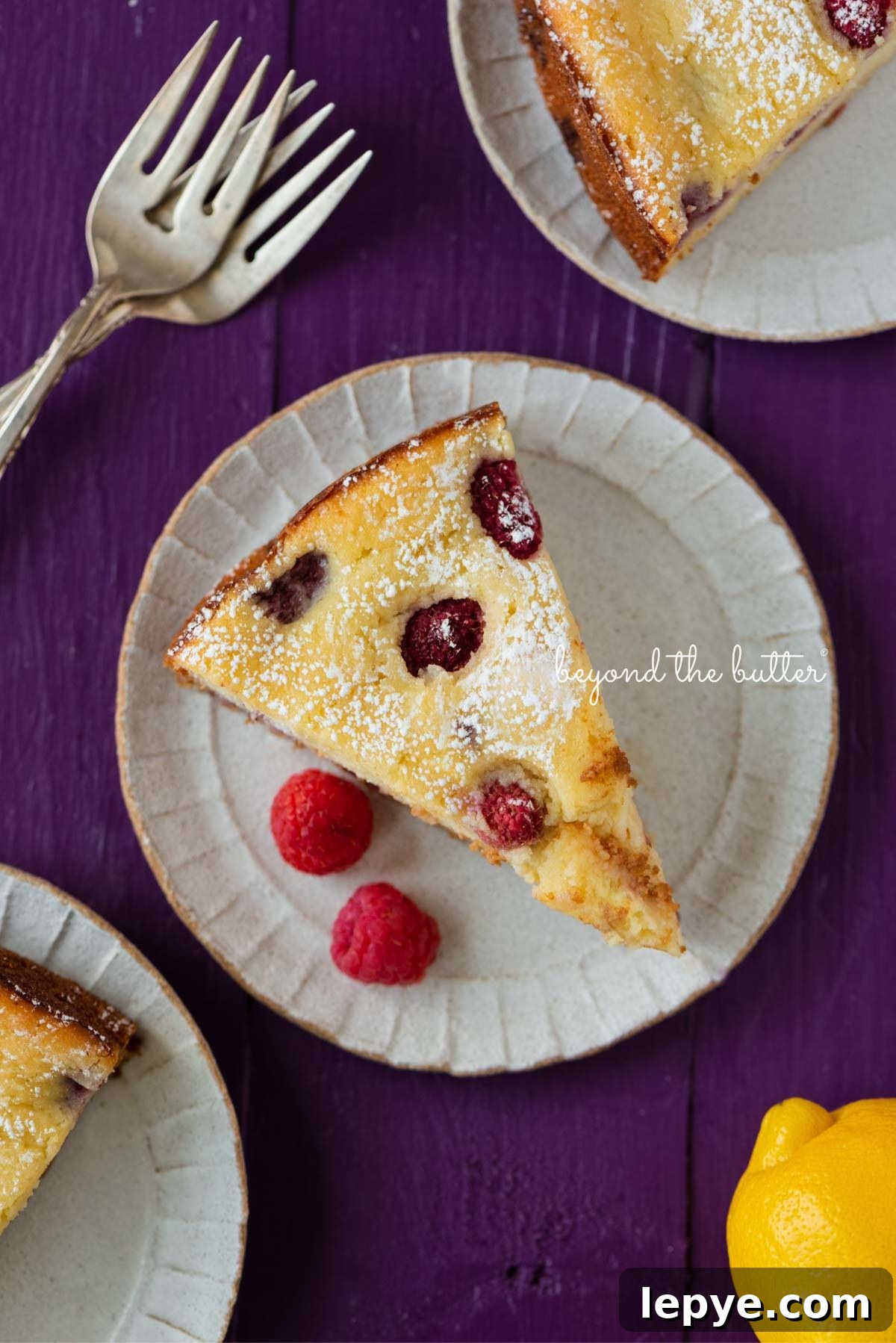 Slices of lemon raspberry ricotta cake dusted with powdered sugar on small ceramic dessert plates and purple wood background.