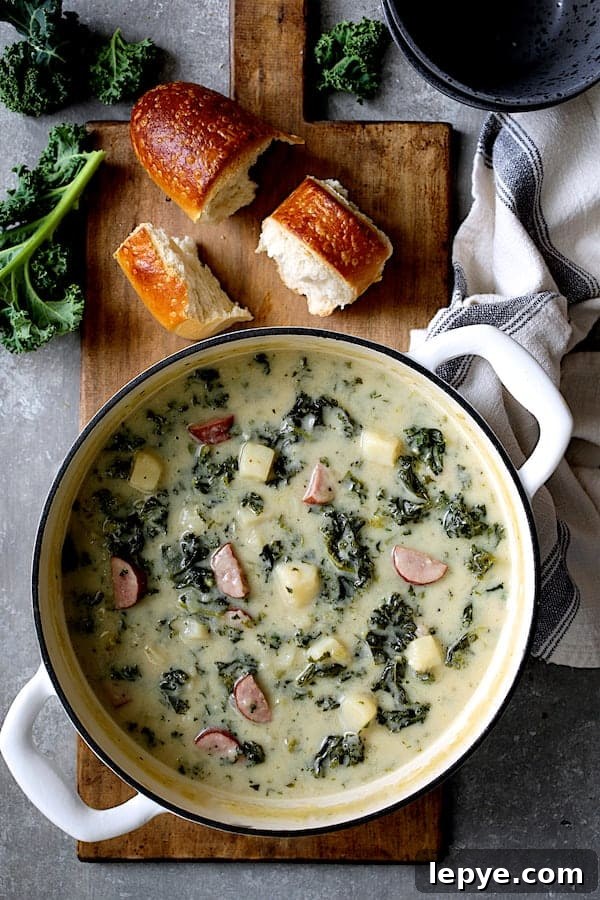 Creamy Kielbasa, Potato & Kale Soup Recipe 2 Photo of Creamy Potato Kielbasa and Kale Soup in white Dutch oven with bread and fresh kale.