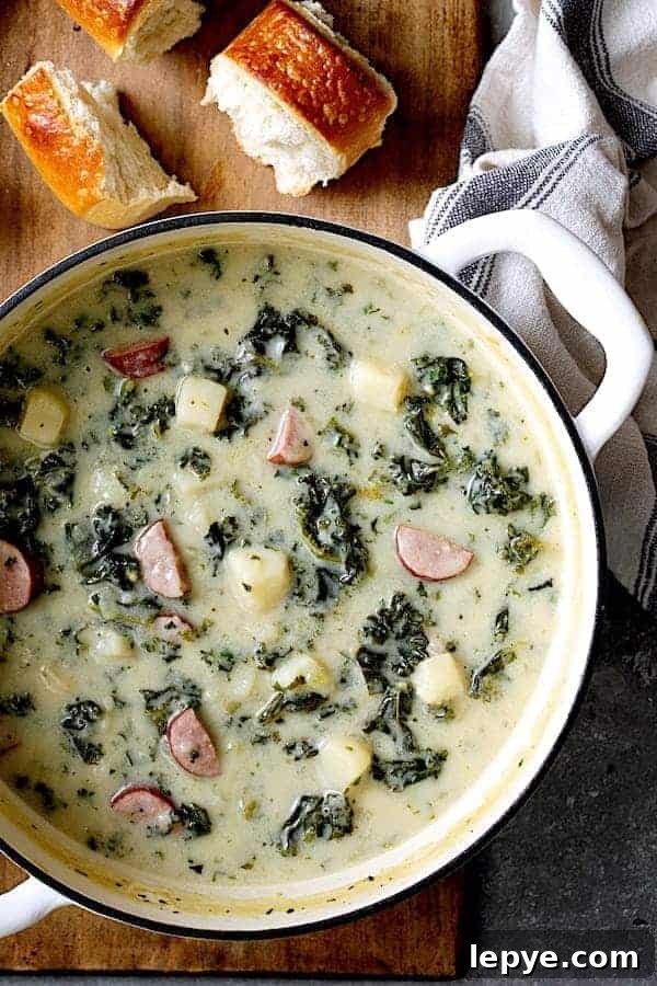Creamy Kielbasa, Potato & Kale Soup Recipe 4 Photo of Creamy Potato Kielbasa and Kale Soup in white Dutch oven with bread on a cutting board.