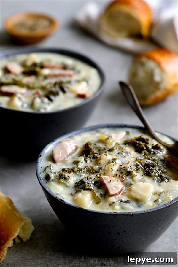 Creamy Kielbasa, Potato & Kale Soup Recipe 5 Photo of two servings of Creamy Potato Kielbasa and Kale Soup in gray bowls with bread scattered about.