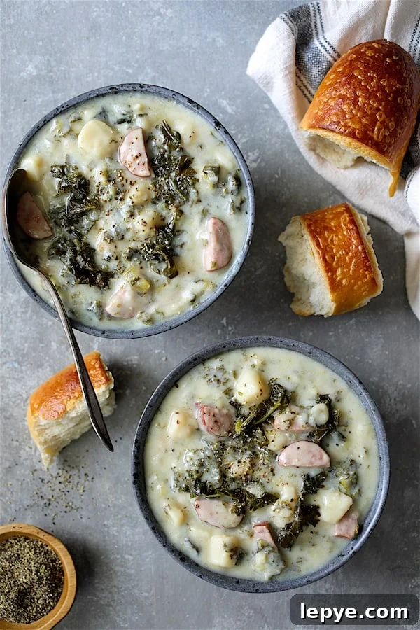 Creamy Kielbasa, Potato & Kale Soup Recipe 6 Photo of two servings of Creamy Potato Kielbasa and Kale Soup in gray bowls with bread scattered about.