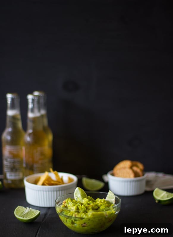 Spicy guacamole in a glass bowl with two bottles of beer in the background.