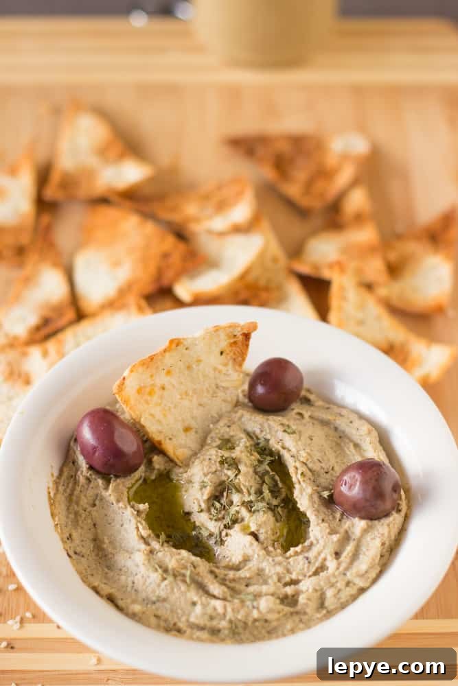 A bowl of baba ganoush with olives and pita chips in it.
