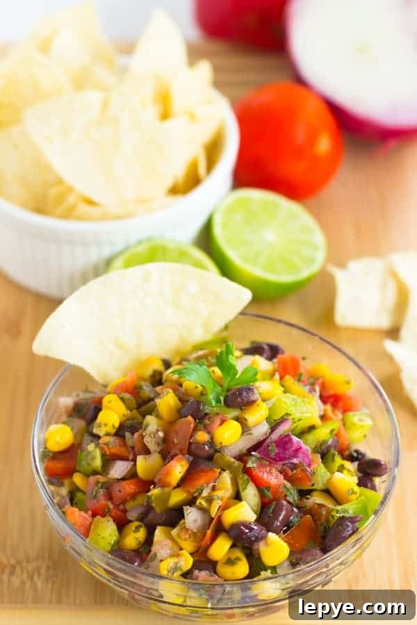 A glass bowl full of black bean salsa with a chip dipped in and lime in the background.