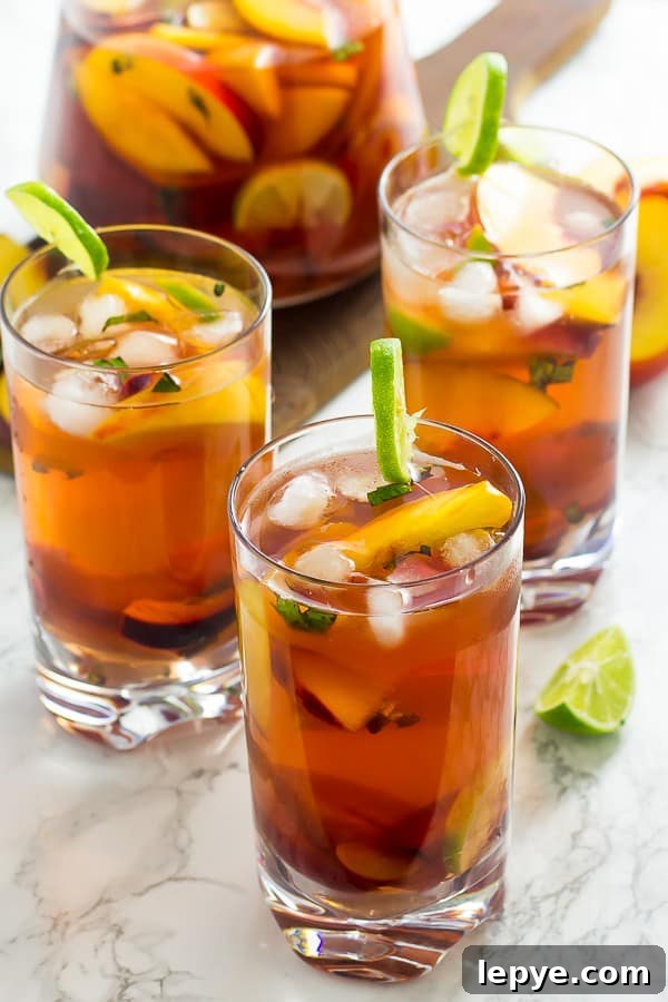 Three glasses of stone fruit sangria with slices of lime.