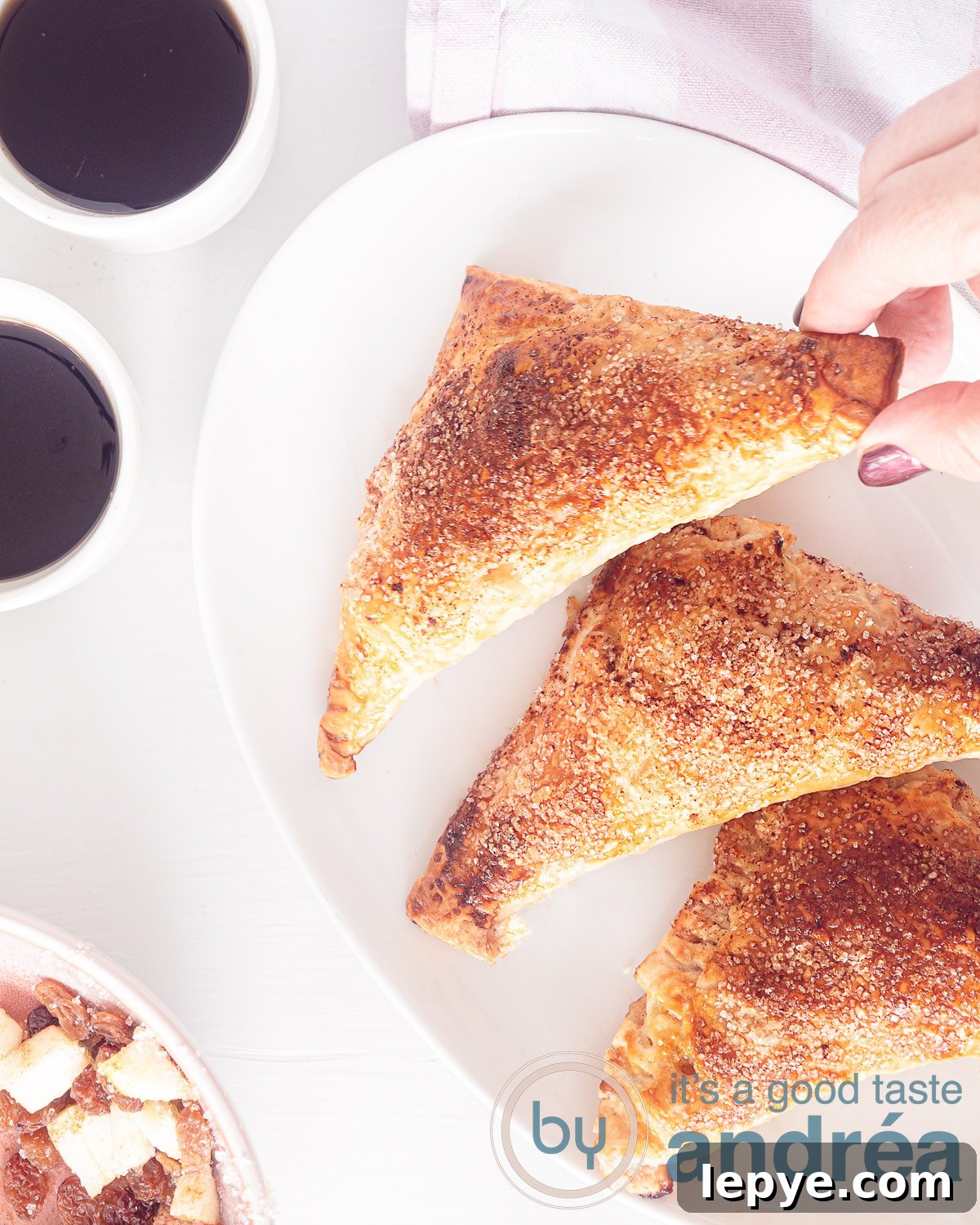 Dutch Appelflappen (Apple Turnovers) — Traditional Recipe & Tips 2 A photo taken from above of a white bowl with three apple turnovers, two white mugs with coffee on a white background
