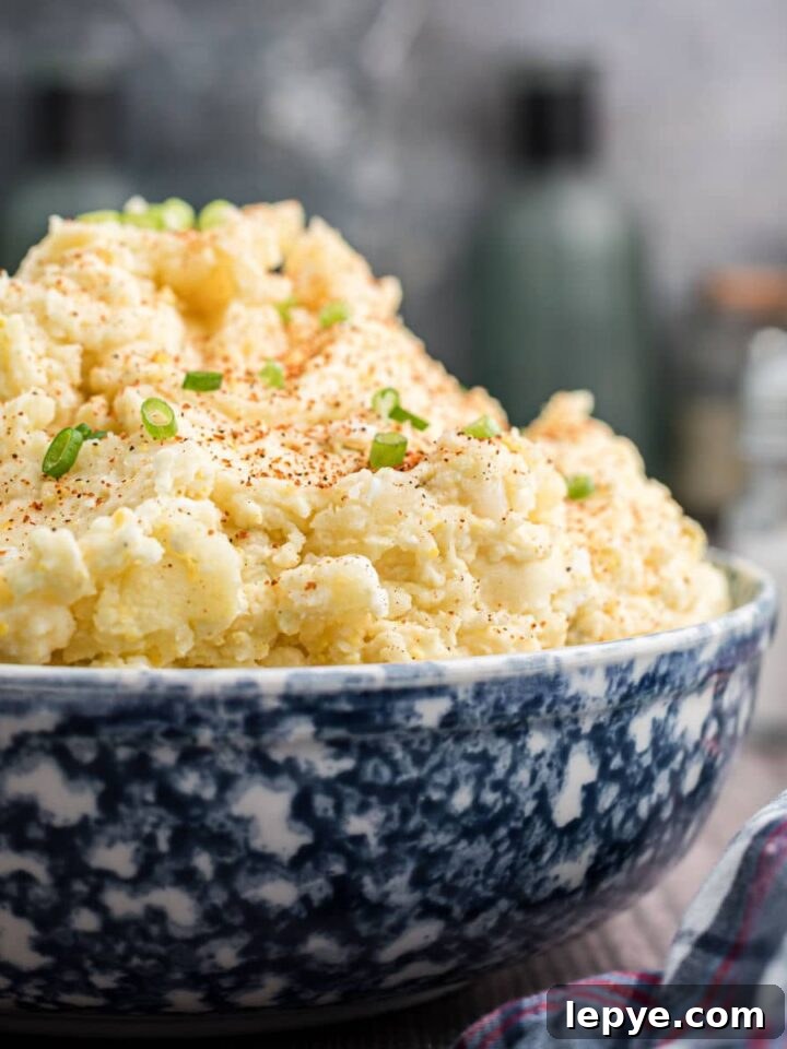 a close up image of a large bowl of Cajun potato salad with green onions sprinkled on top