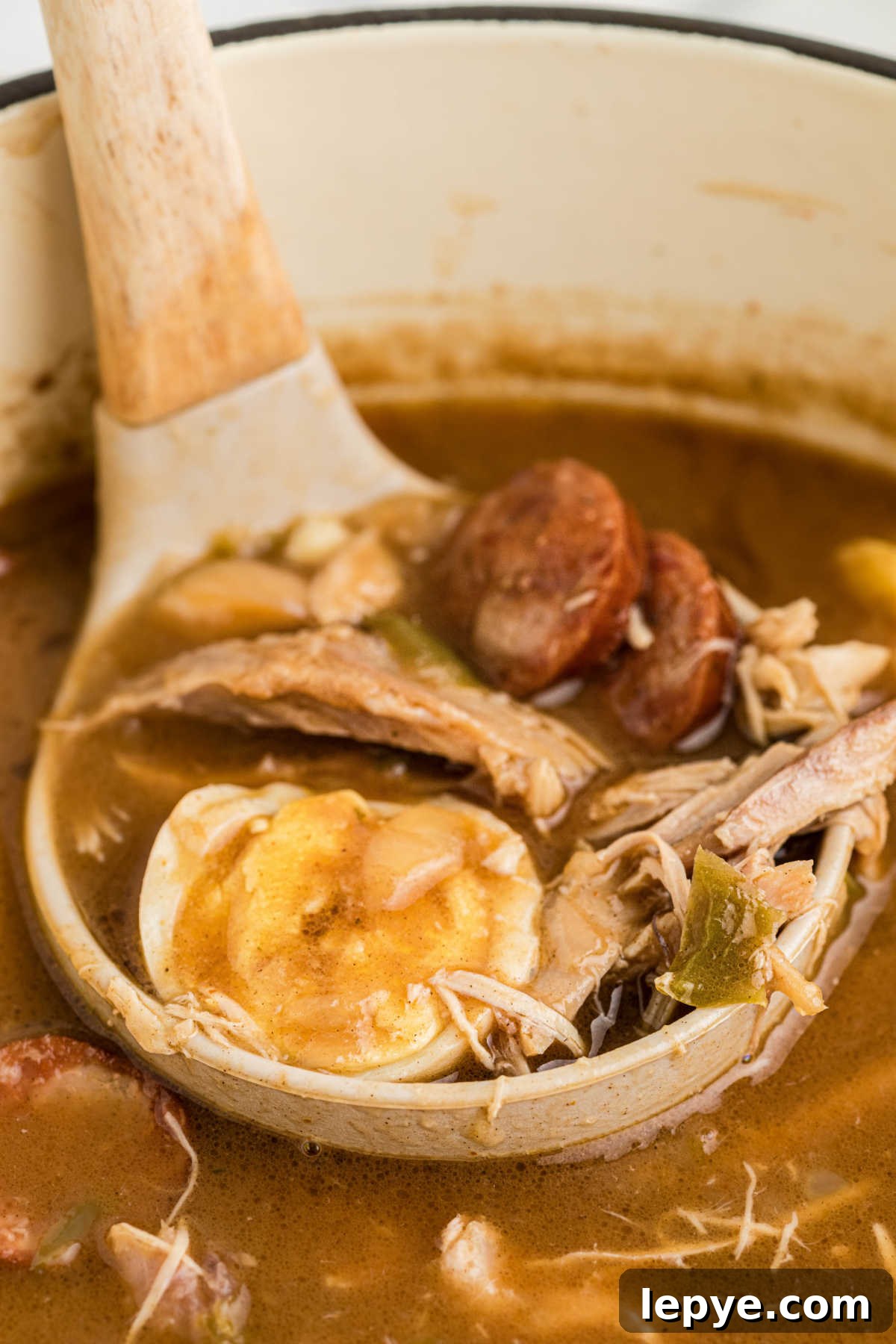 A ladle lifting out from a leftover turkey and andouille gumbo, with a boiled egg.
