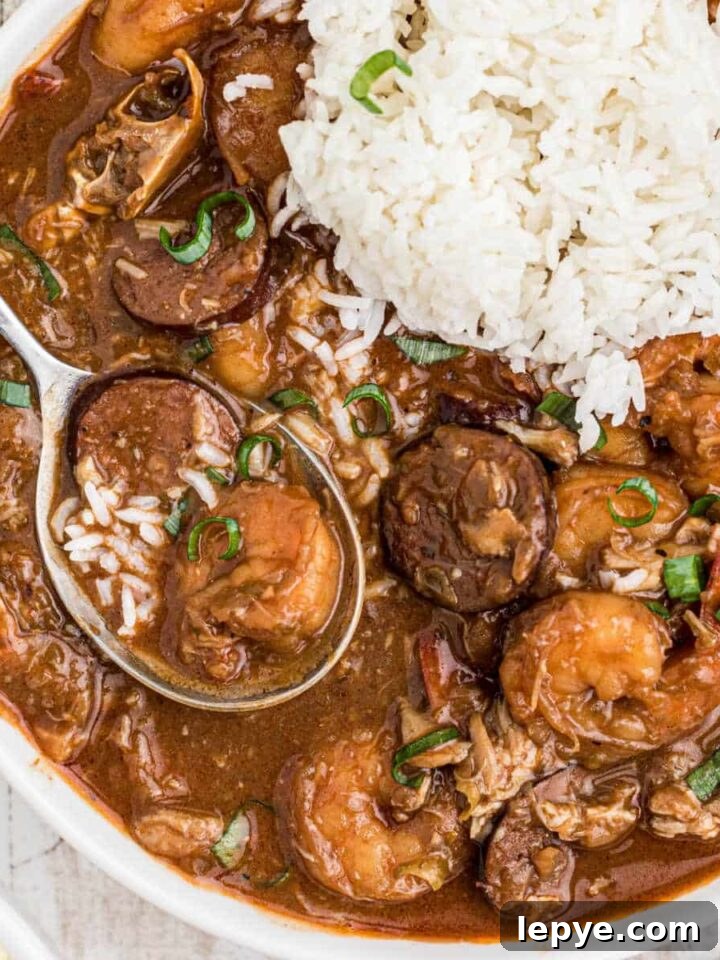 Close up of a bowl of seafood gumbo with a pile of rice and a spoon digging into it.