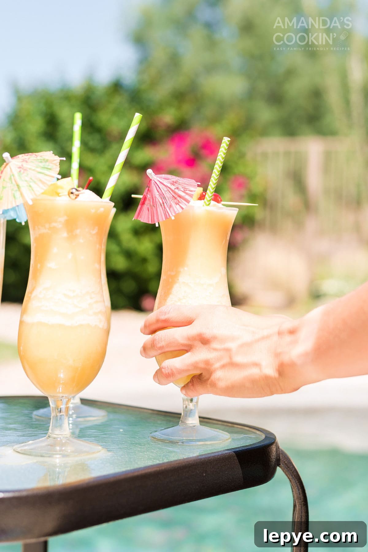 hand reaching for and picking up a pina colada cocktail by the pool