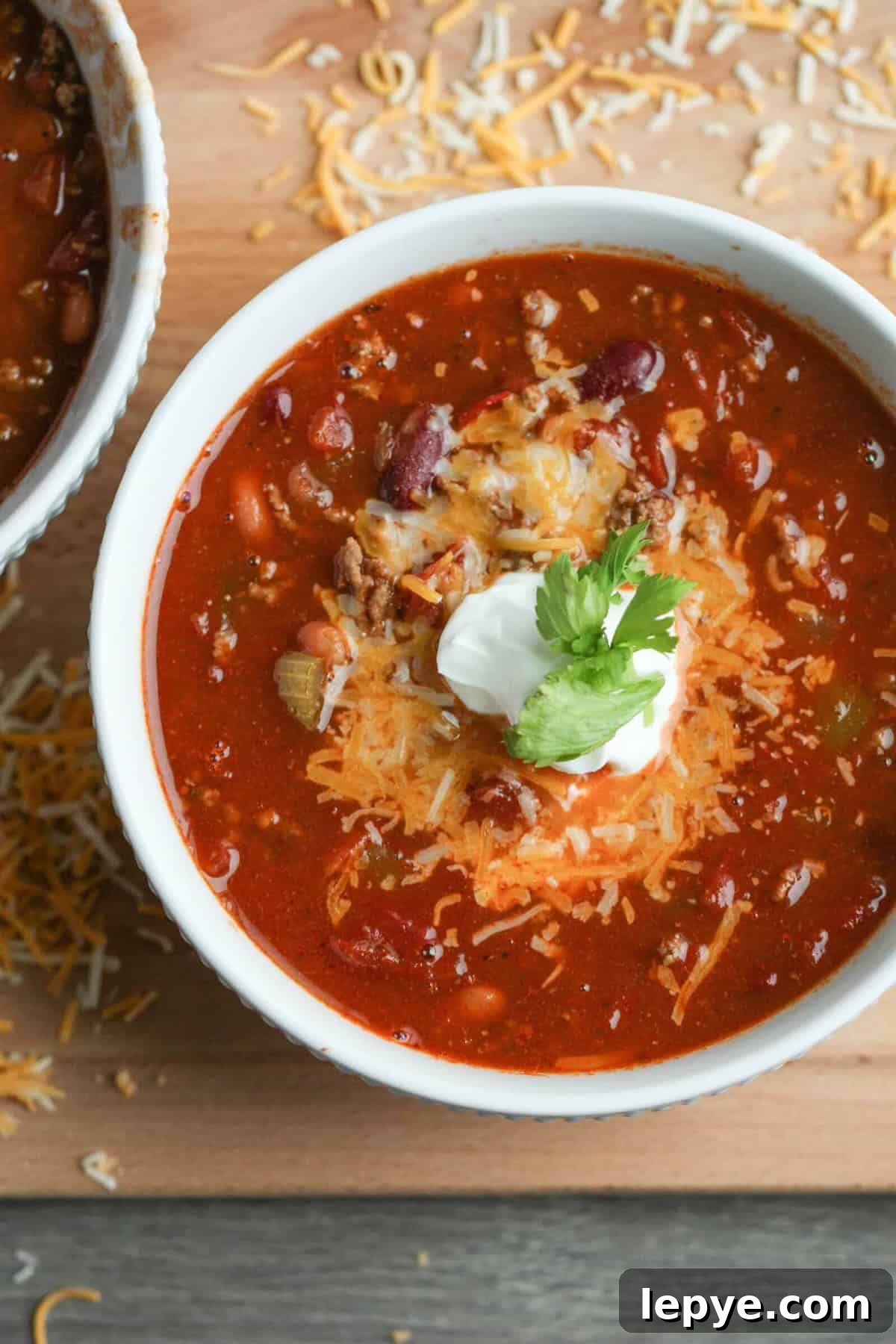 Freezer Meal Planning for Large and Small Families 2 A bowl of chili topped with shredded cheese, a dollop of sour cream, and a sprig of cilantro, with scattered cheese on the wooden surface nearby.