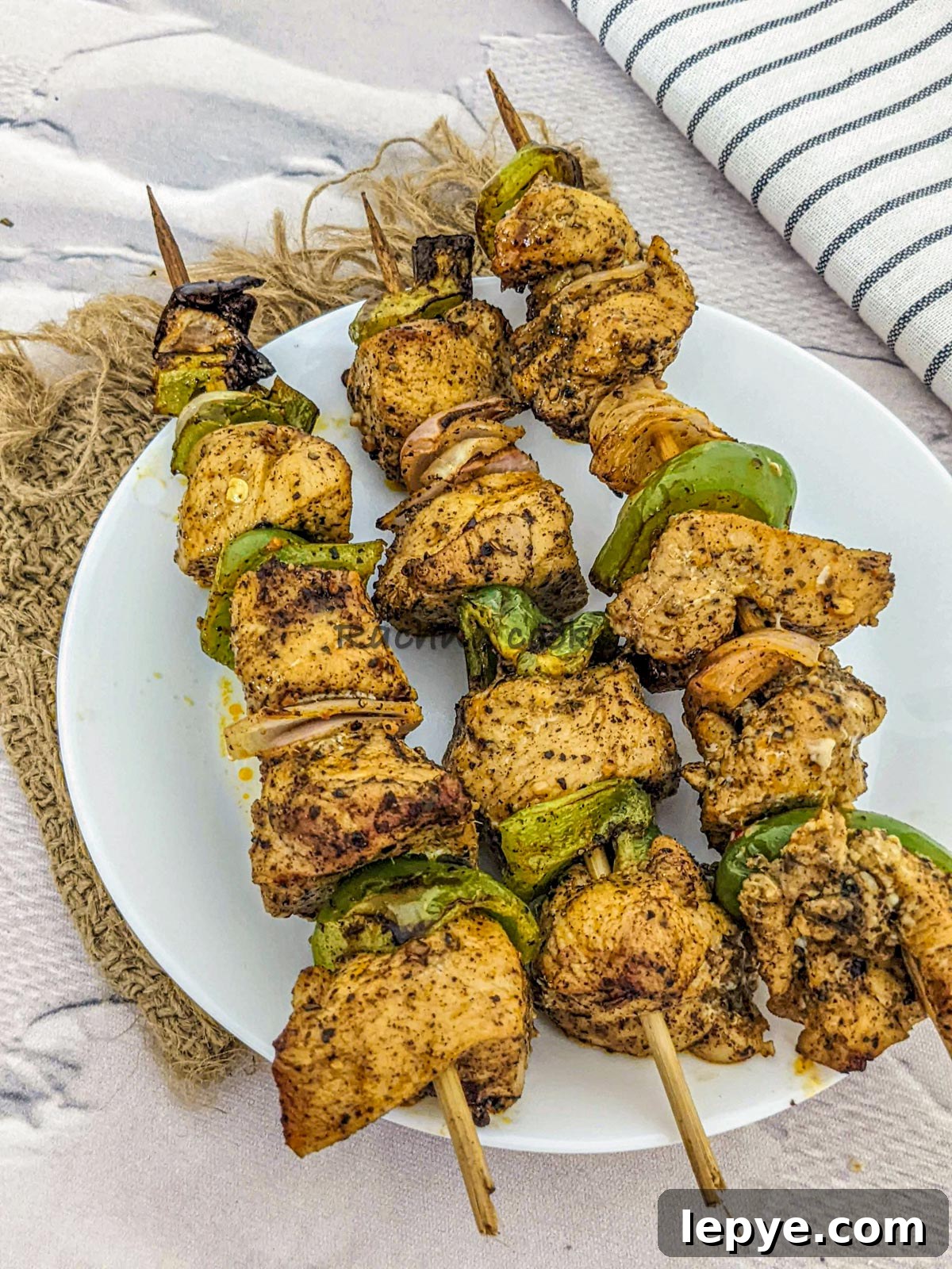 3 skewers of chicken kabobs after air frying served on a white plate.