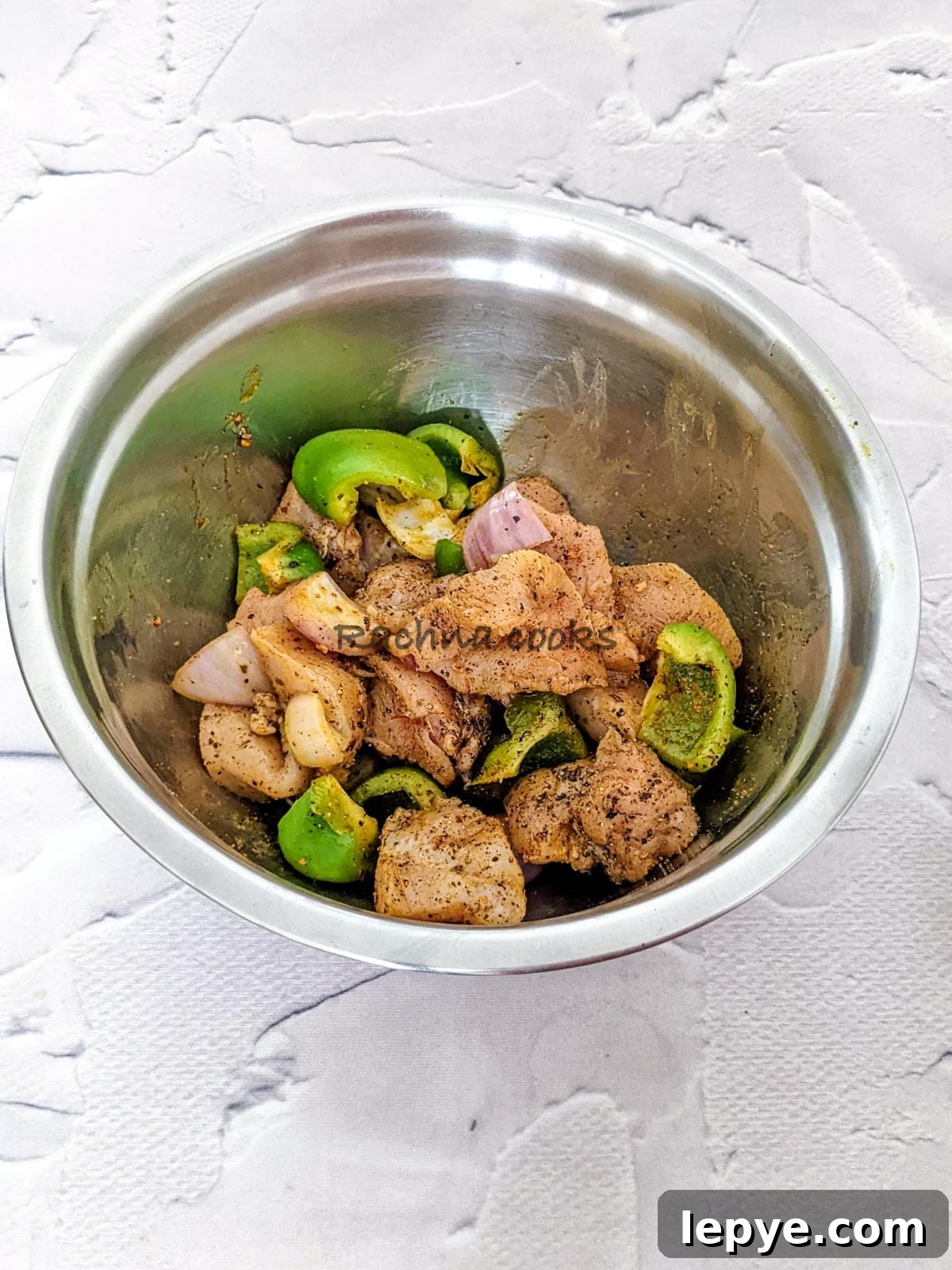 Chicken and veggies marinated in spices and oil in a steel bowl