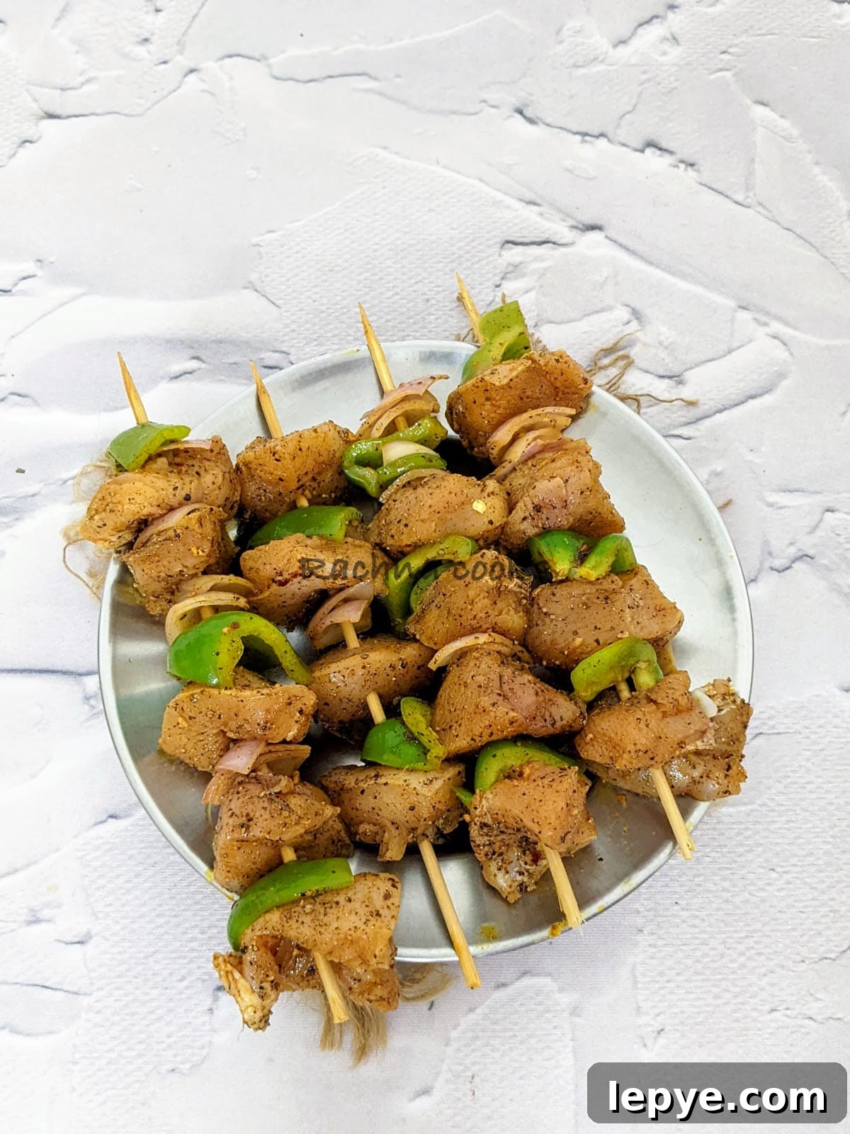 4 skewers of threaded cubed chicken and veggies ready to air fry on a steel plate.