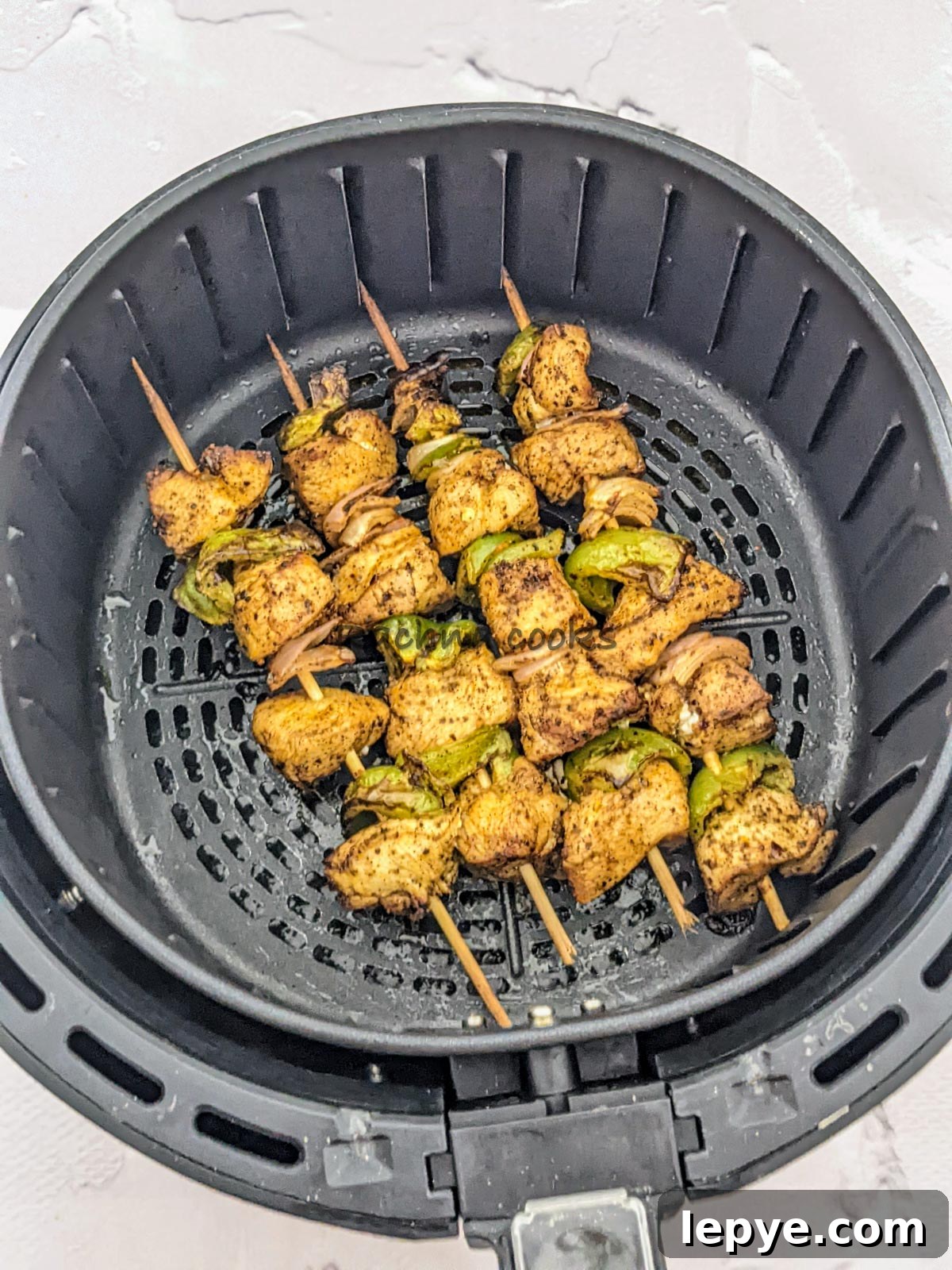 4 skewers of chicken kabob after air frying in air fryer basket.