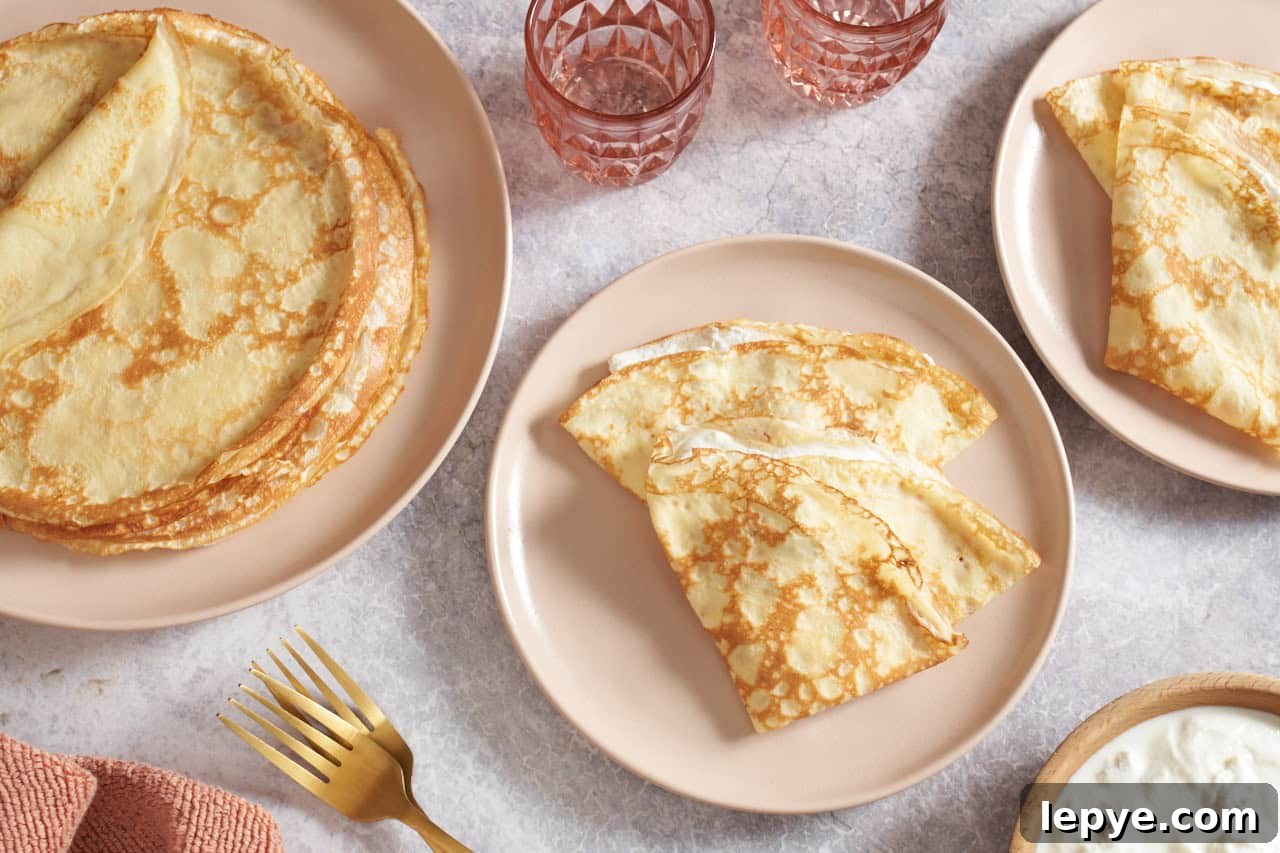 Sweet Nalysnyky: Classic Ukrainian Crepes with Cottage Cheese Filling 2 One large plate of stacked crepes, two small plates of Ukrainian crepes filled with ricotta cheese and raisins, two pink glasses are at the top of the photo.