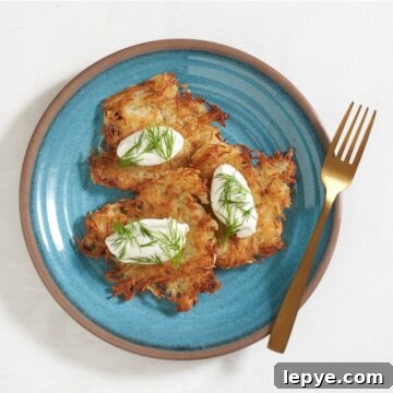 Ukrainian potato pancakes (deruny) topped with sour cream and dill on a blue plate, a gold fork is on the right.