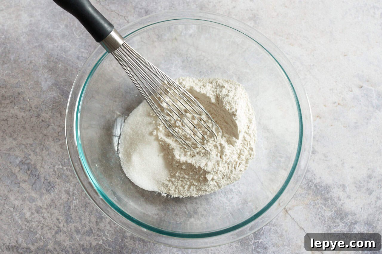 Sweet Nalysnyky: Classic Ukrainian Crepes with Cottage Cheese Filling 4 A glass bowl of flour and sugar with a whisk in it.