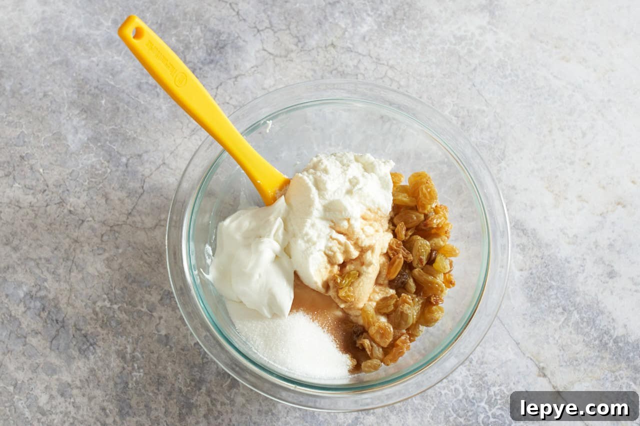Sweet Nalysnyky: Classic Ukrainian Crepes with Cottage Cheese Filling 5 A yellow spatula in a mixing bowl full of ricotta cheese, raisins and other ingredients to make a crepe filling.