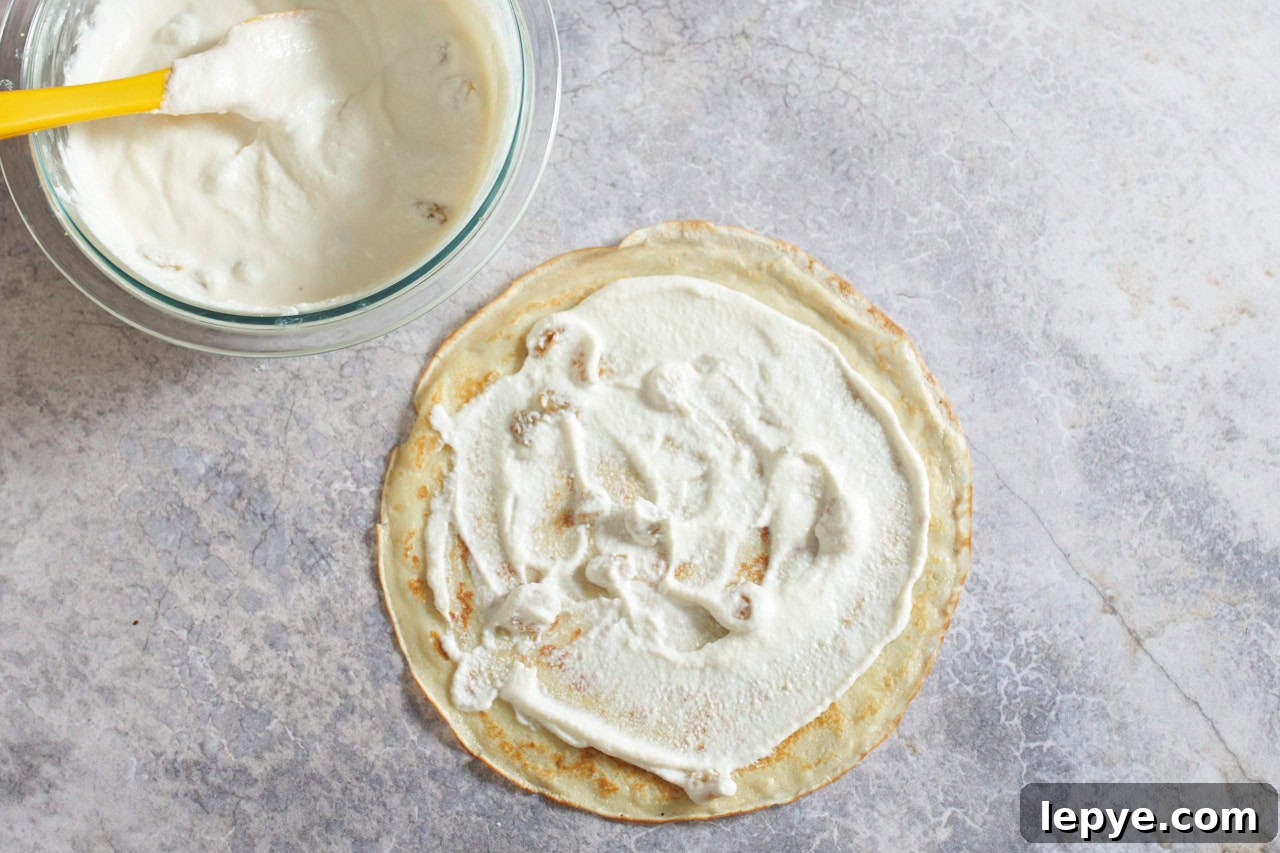 Sweet Nalysnyky: Classic Ukrainian Crepes with Cottage Cheese Filling 7 A crepe with ricotta cheese filling spread on it, a bowl of filling is in the upper left.