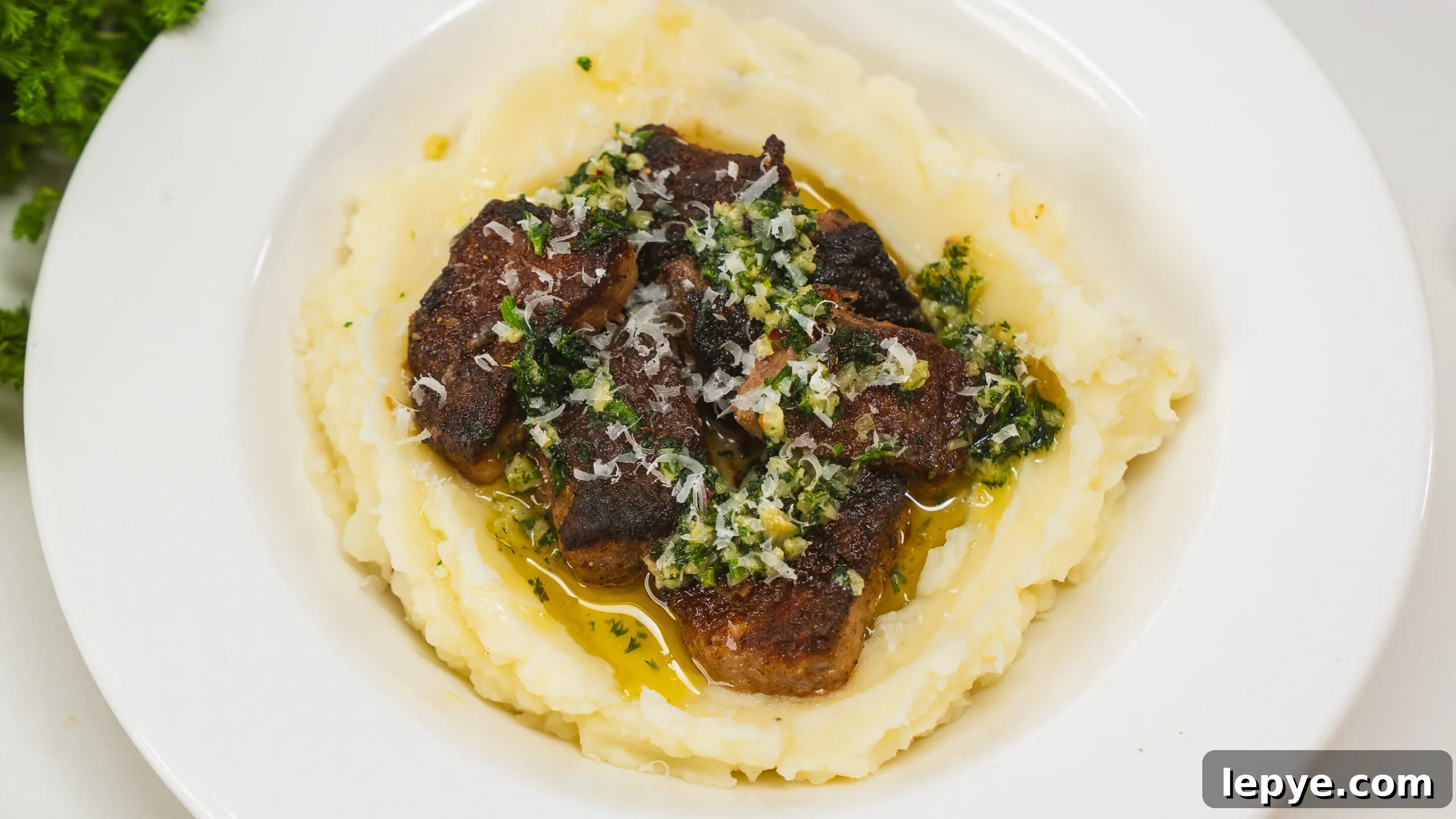 Garlic butter steak bites served over mashed potatoes in a white bowl.