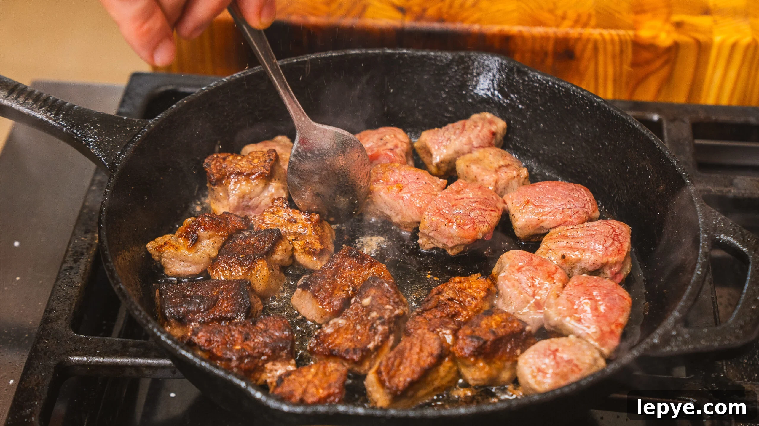 Steak bites being seared in a cast iron pan.