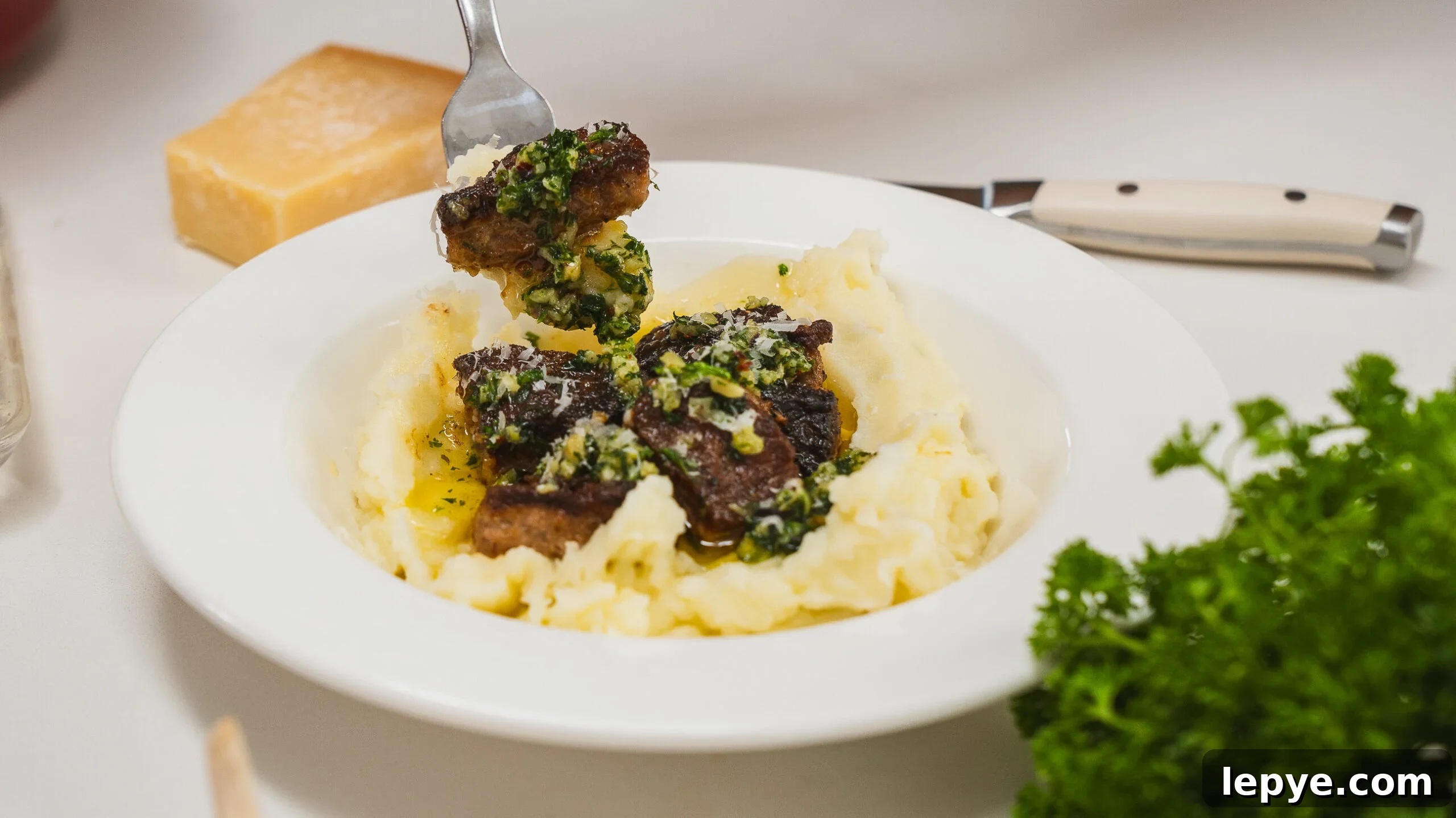 Garlic butter steak bites in a white bowl served over mashed potatoes.