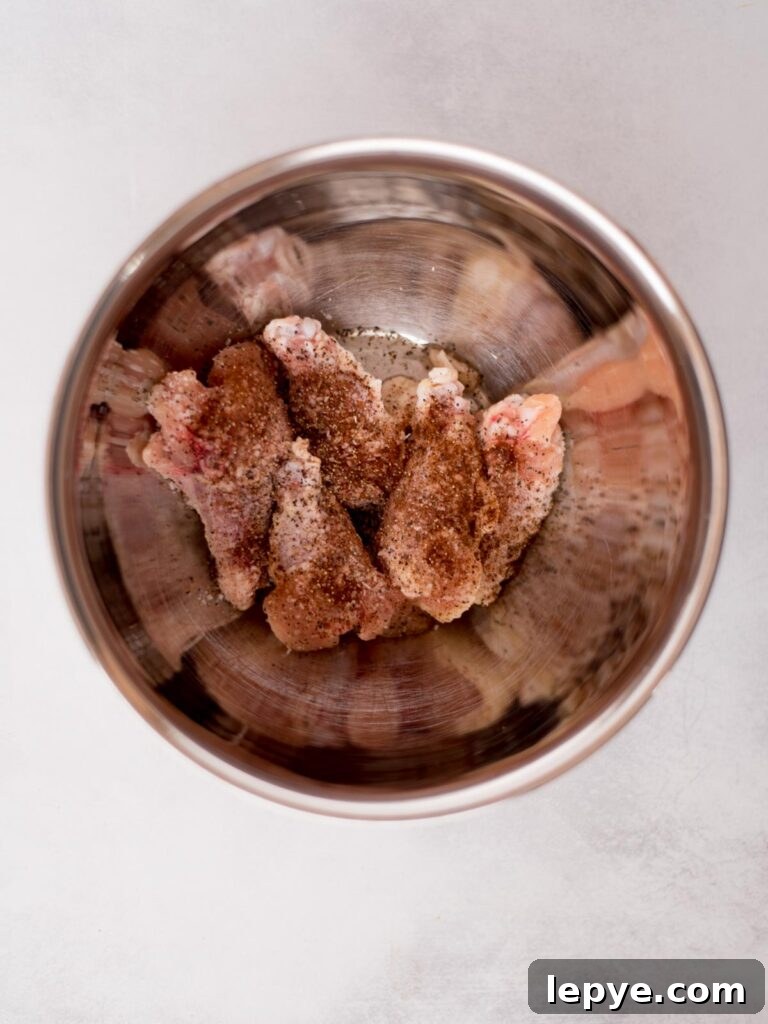 Citrus Tequila-Lime Chicken Wings Recipe for Game Day 4 Raw chicken wings with seasonings added over them in a mixing bowl ready to combine.