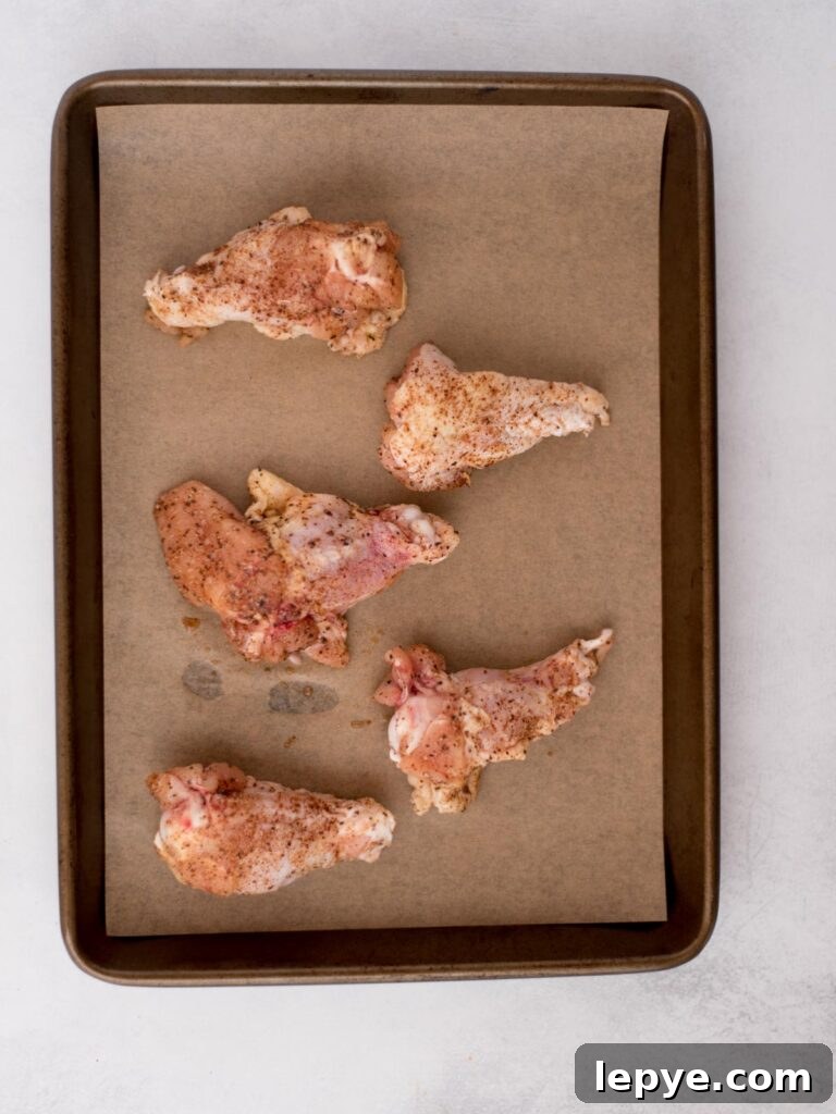 Citrus Tequila-Lime Chicken Wings Recipe for Game Day 5 Seasoned raw chicken wings laying on parchment paper covered baking sheet.
