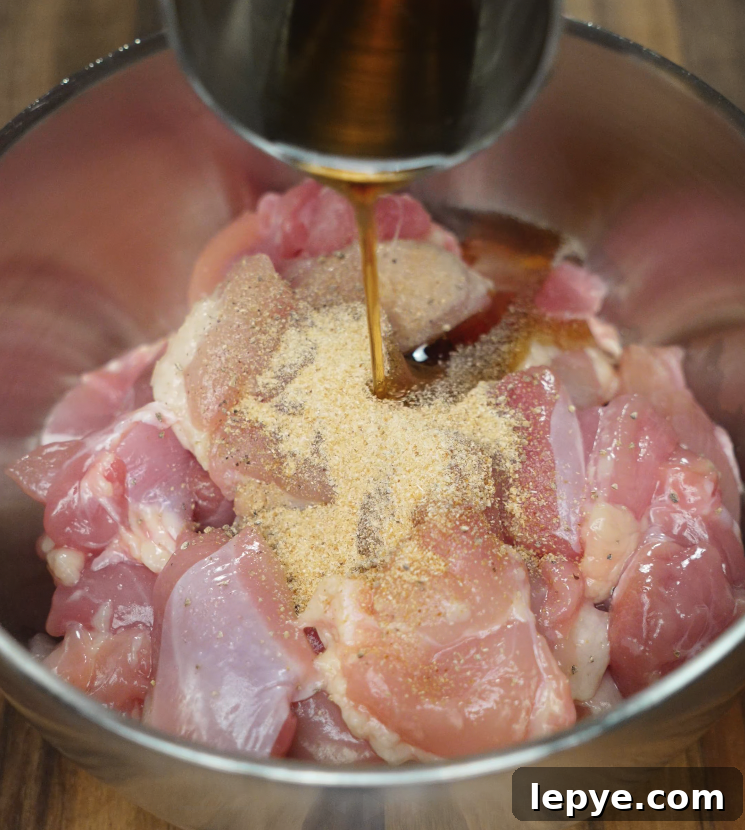 Soy sauce being poured over raw chicken with garlic powder in a metal mixing bowl for marinating.