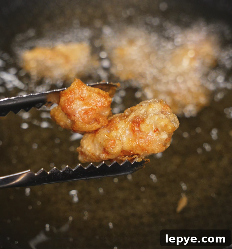 Close-up of crispy golden brown fried chicken being lifted from hot oil with tongs during frying process.