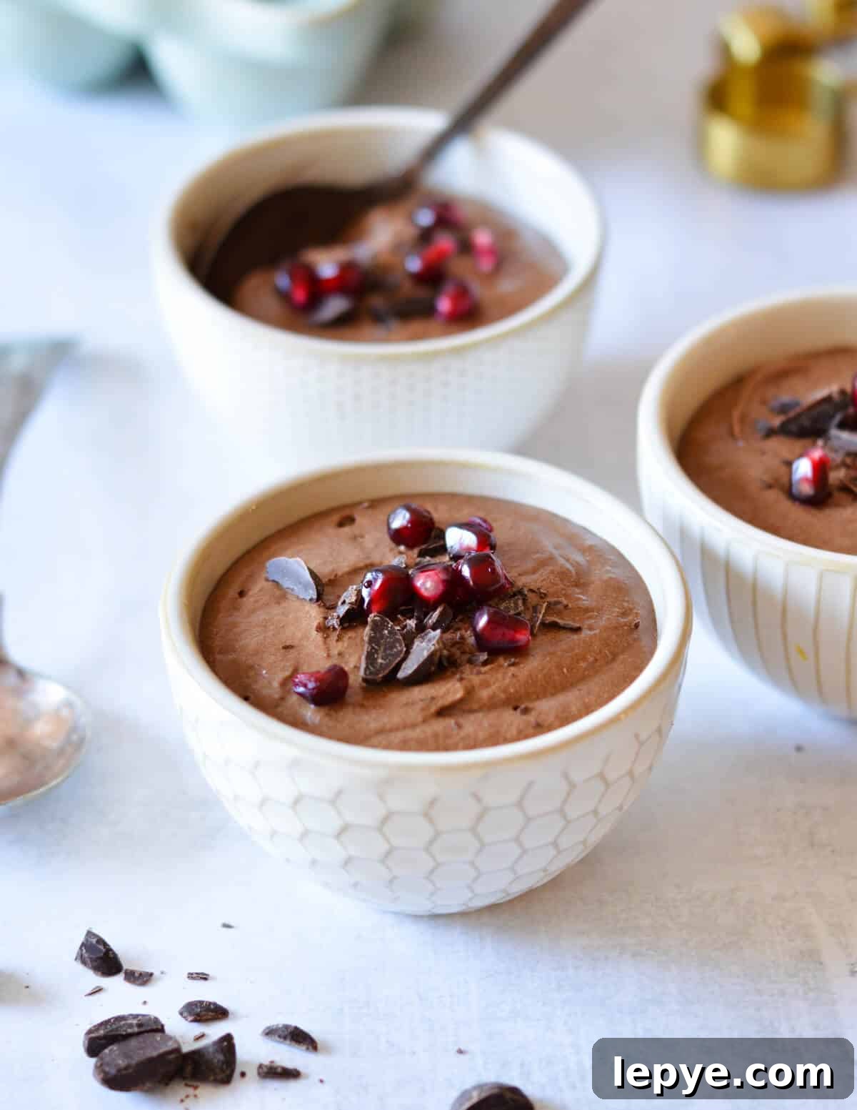 Decadent Chocolate Mousse Recipe for Silky, No-Bake Perfection 20 bowls of chocolate mousse with shaved chocolate and pomegranate seeds on top.