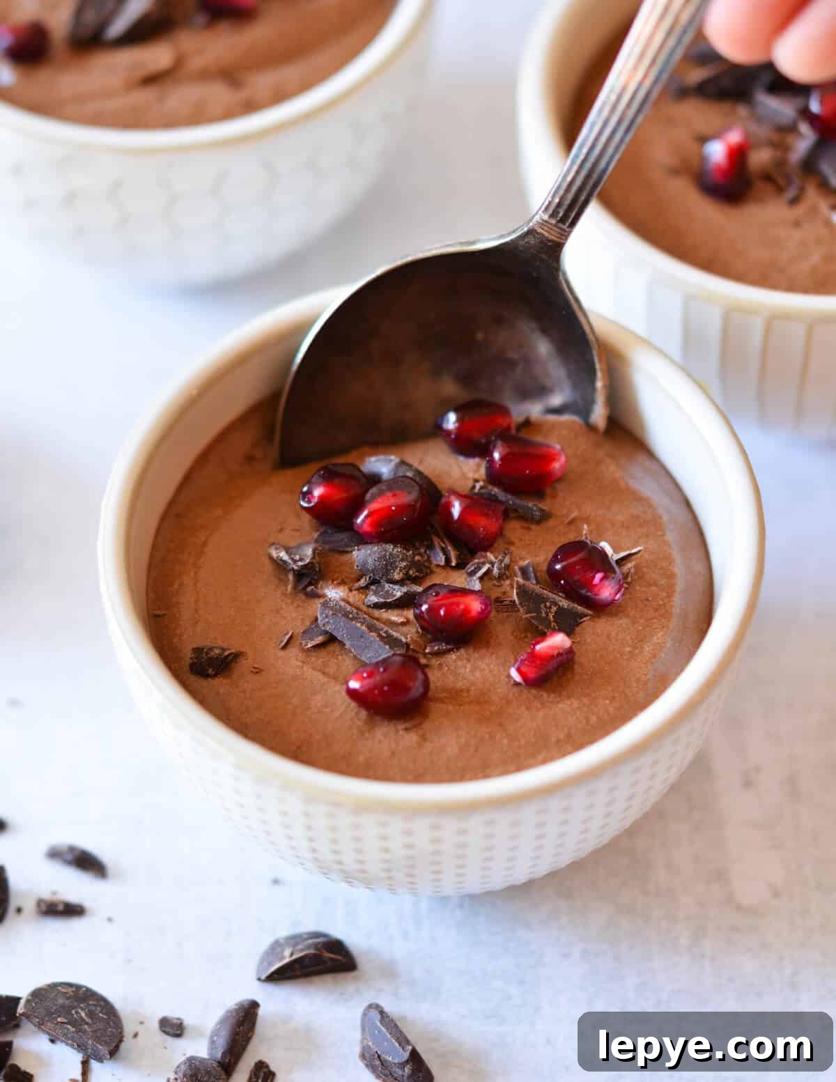 Decadent Chocolate Mousse Recipe for Silky, No-Bake Perfection 3 spoon in a cup of chocolate mousse with pomegranate seeds on top.