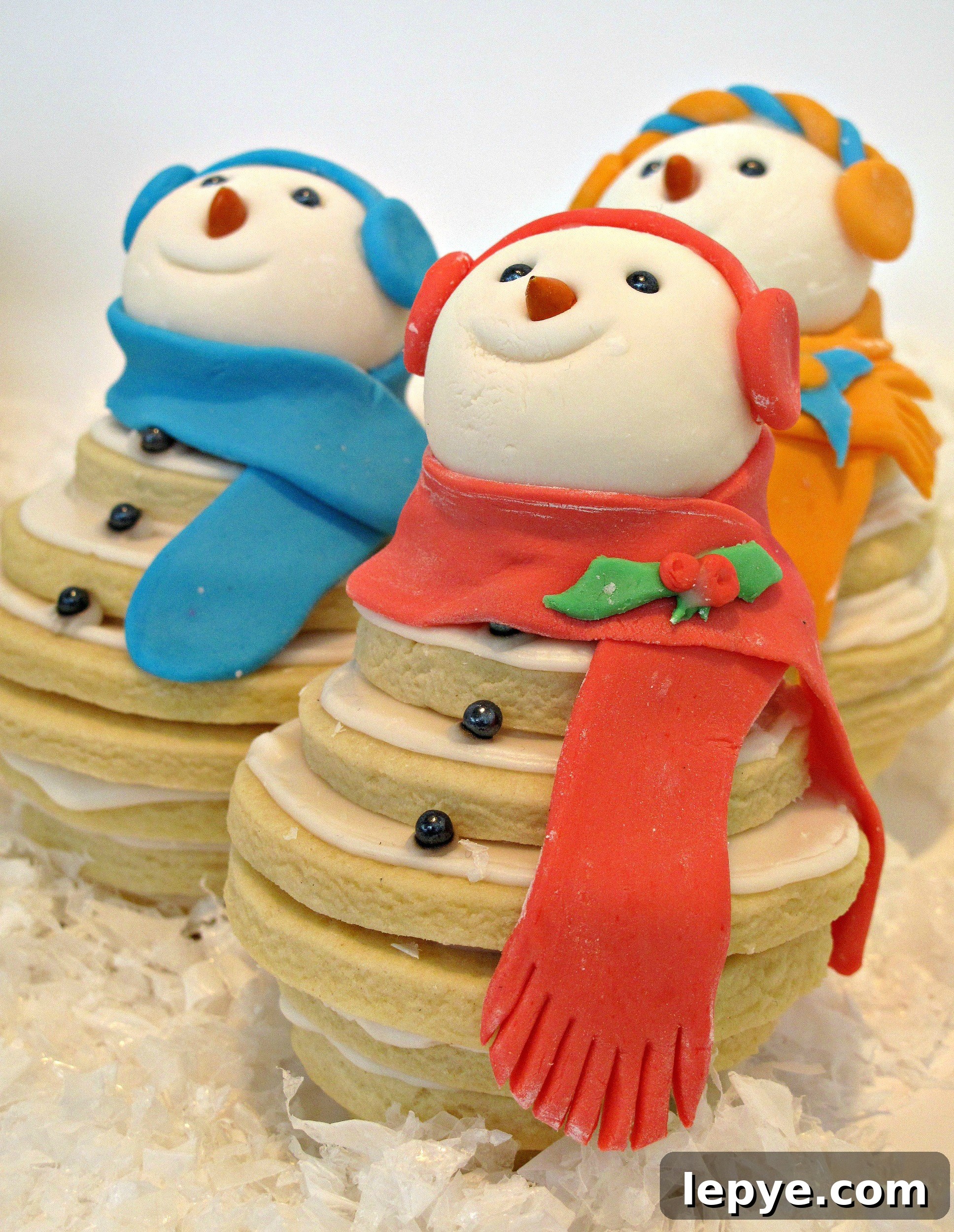 Closeup of a snowman cookie wearing a red scarf and red ear muffs.