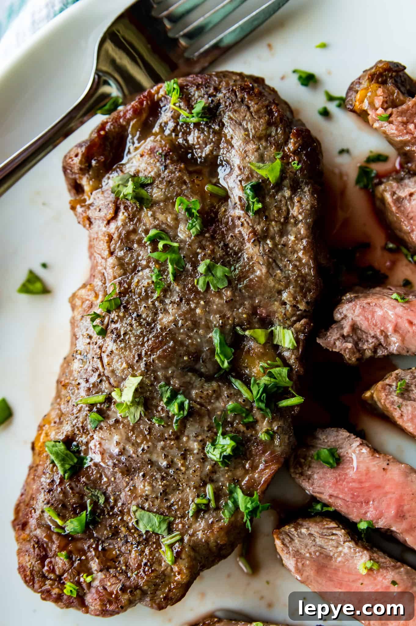 A piece of steak on a plate, seasoned with cilantro with a cut steak next to it.