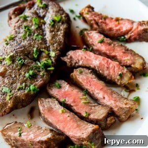 A piece of cut up steak on a plate with a full piece of steak beside it.