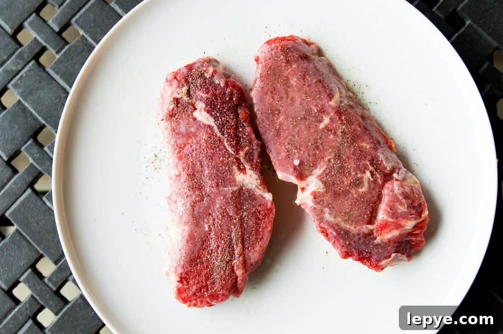 Frozen steaks coated in salt and pepper on a plate.