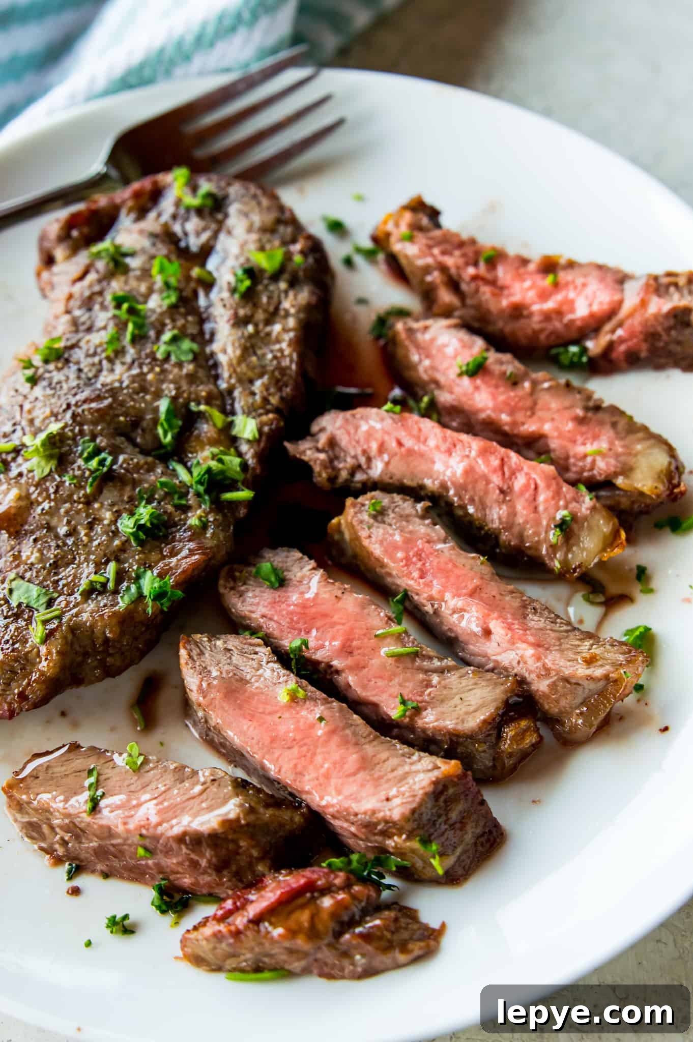 A piece of medium rare cut steak on a plate garnished with fresh chopped parsley.