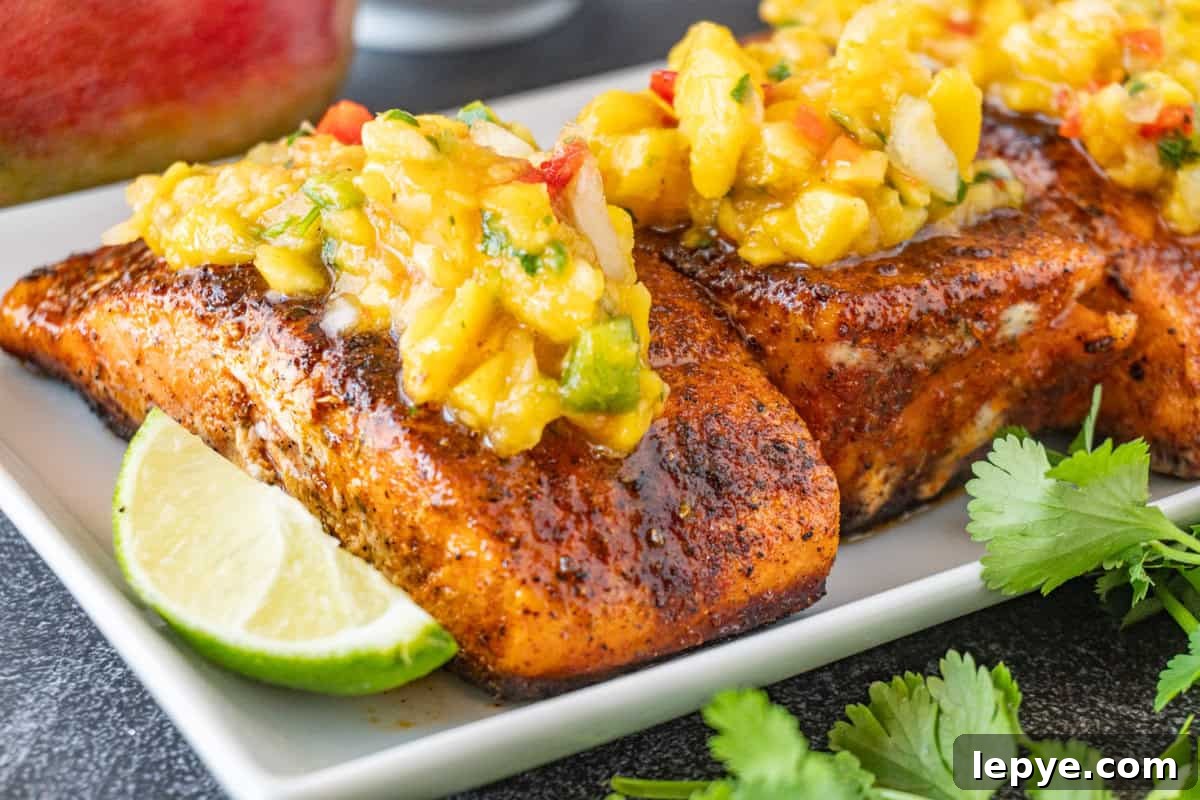 Grilled Salmon with Fresh Mango Salsa Recipe 11 salmon filets on a white plate with lime wedge and topped with mango salsa.