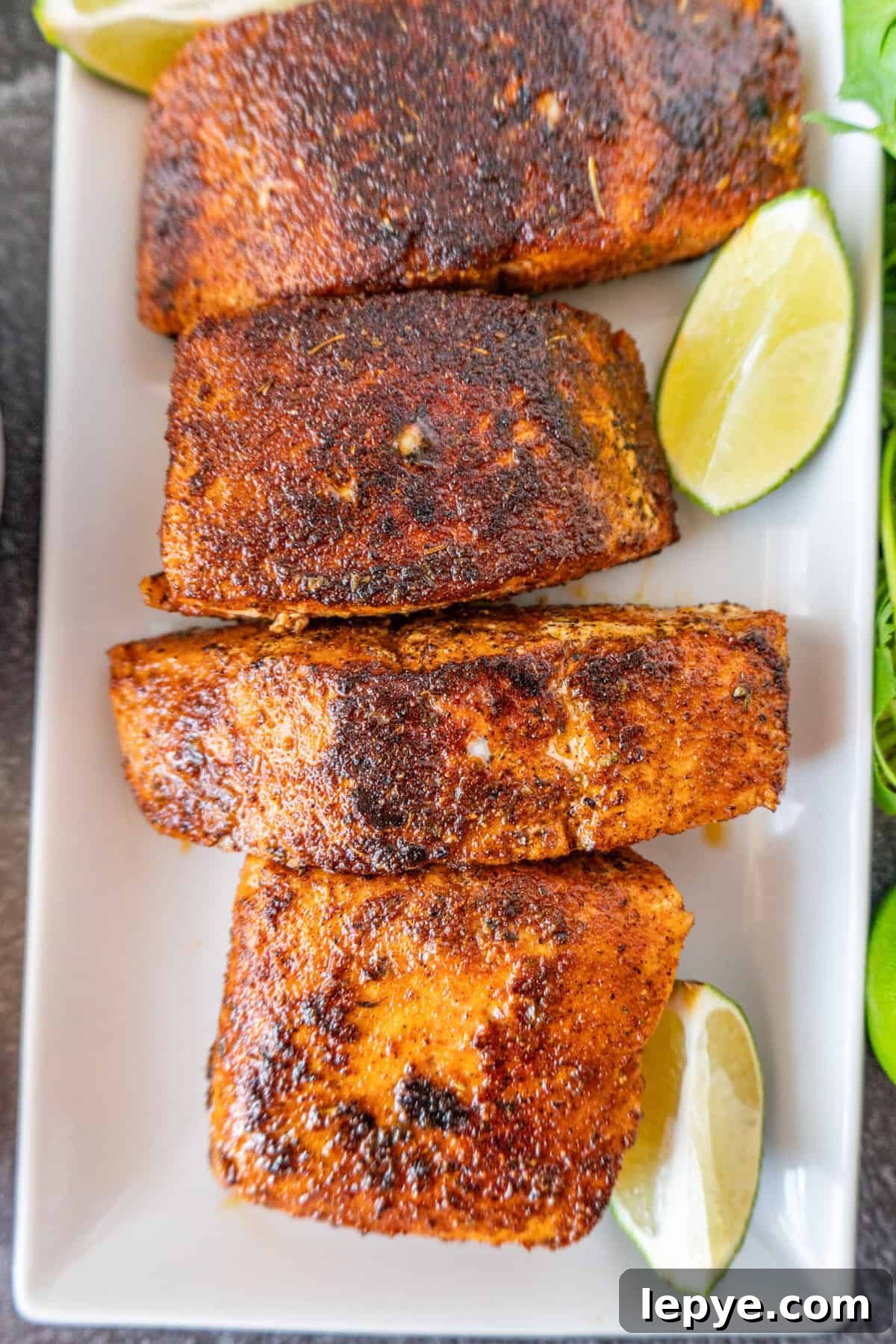 Grilled Salmon with Fresh Mango Salsa Recipe 12 cooked salmon on a white platter with lime wedges nearby.