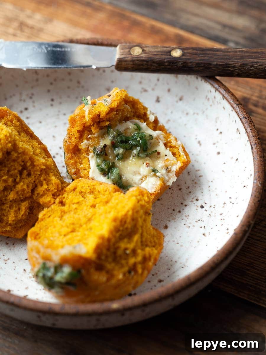 Gluten-Free Pumpkin Dinner Rolls Recipe for Fall Gatherings 8 a pumpkin dinner roll on a plate topped with butter and sage with a small knife in the back