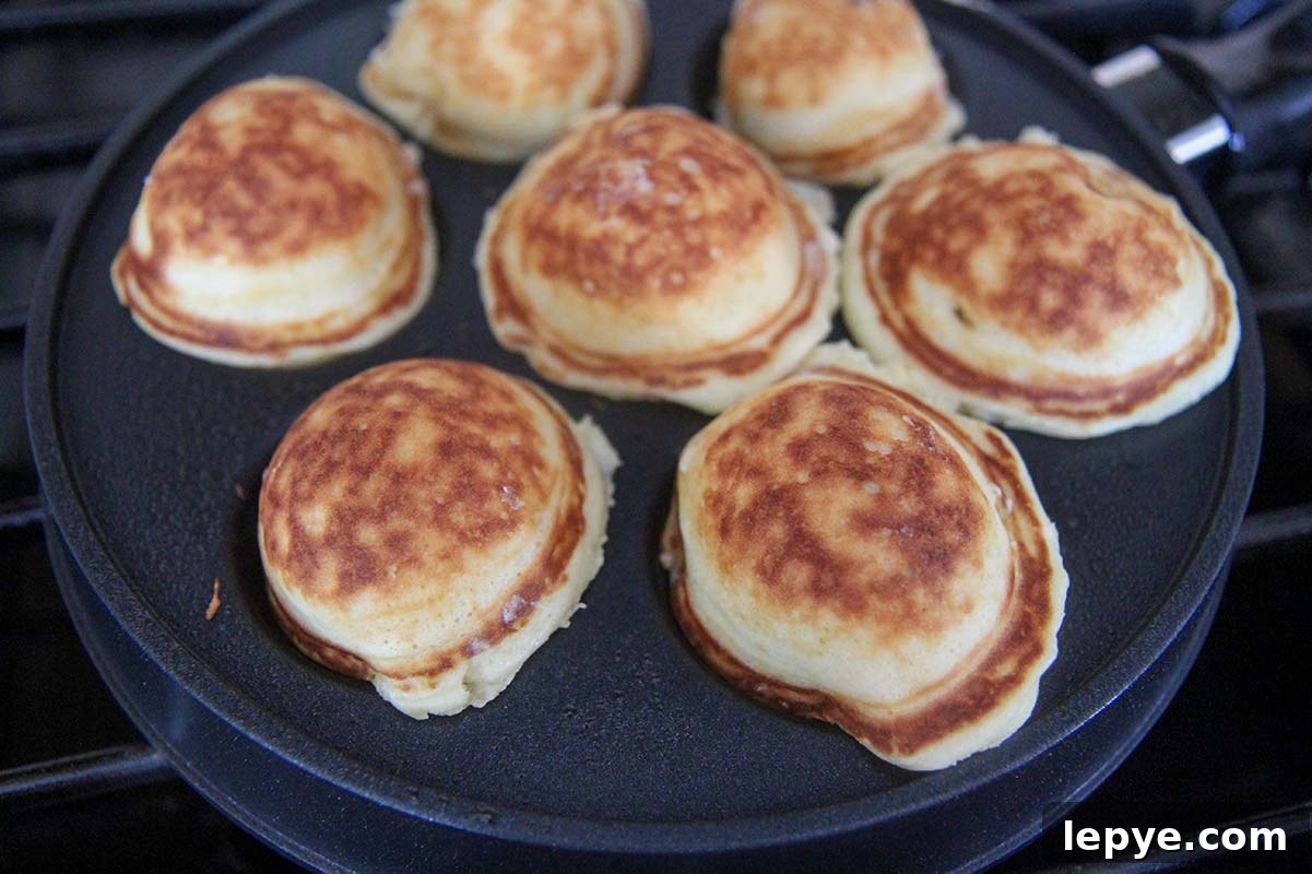 seven mini pancakes cooking in a pan.